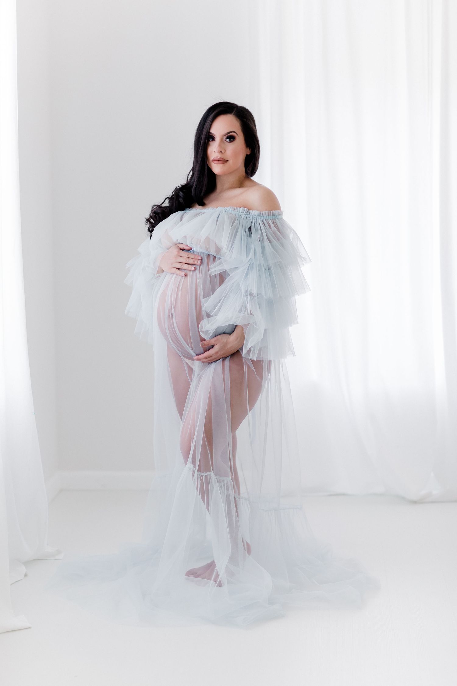 Ethereal studio portrait with sheer ice blue tulle gown and dramatic lighting.