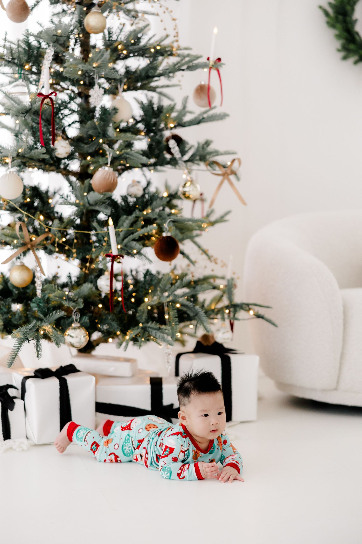 A decorated Christmas tree with white and gold ornaments stands in a minimalist studio setting.