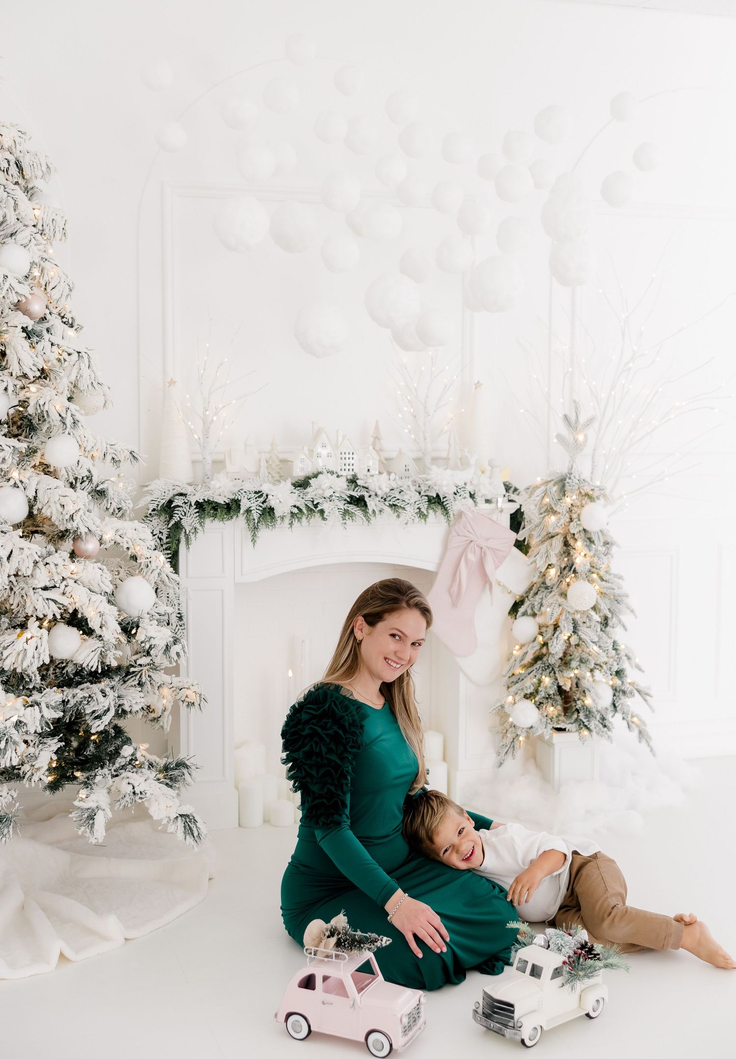 Holiday photo session with flocked Christmas trees and vintage toy car in white studio setting.