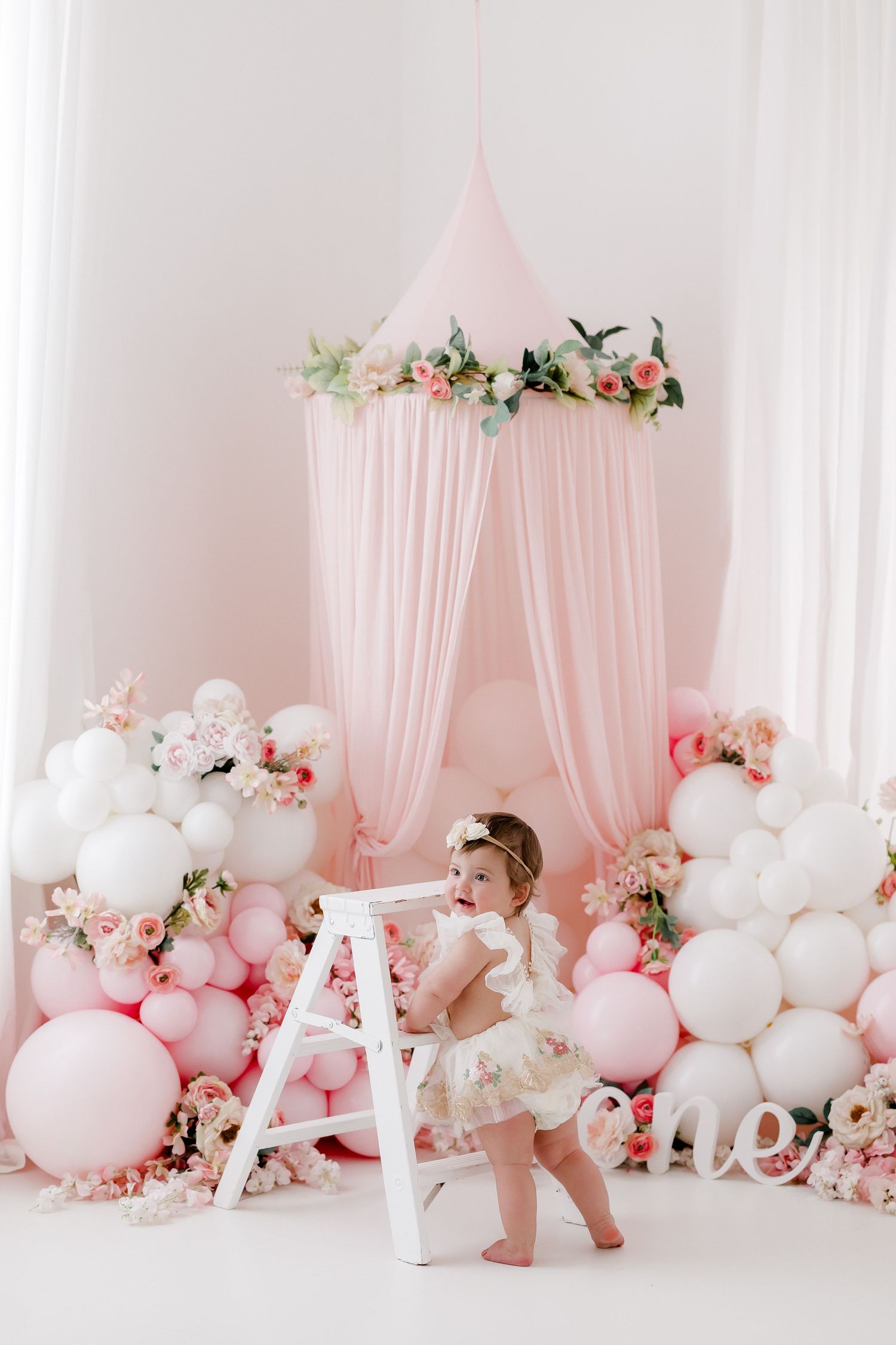 Pink canopy tent with floral decor and balloon arch in romantic first birthday setup.