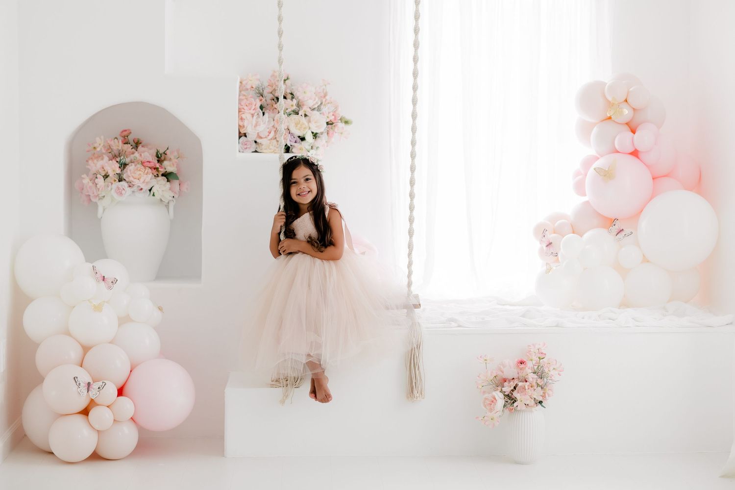 Elegant white photo studio with pink balloon decorations and floral arrangements creating a romantic atmosphere.