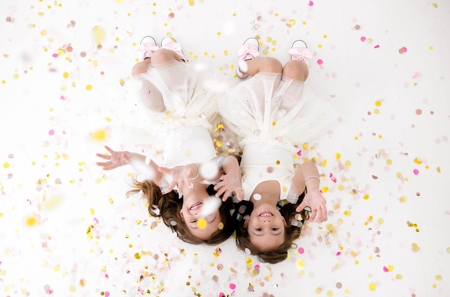 Two people lying on white background with colorful confetti scattered around them in creative portrait composition.