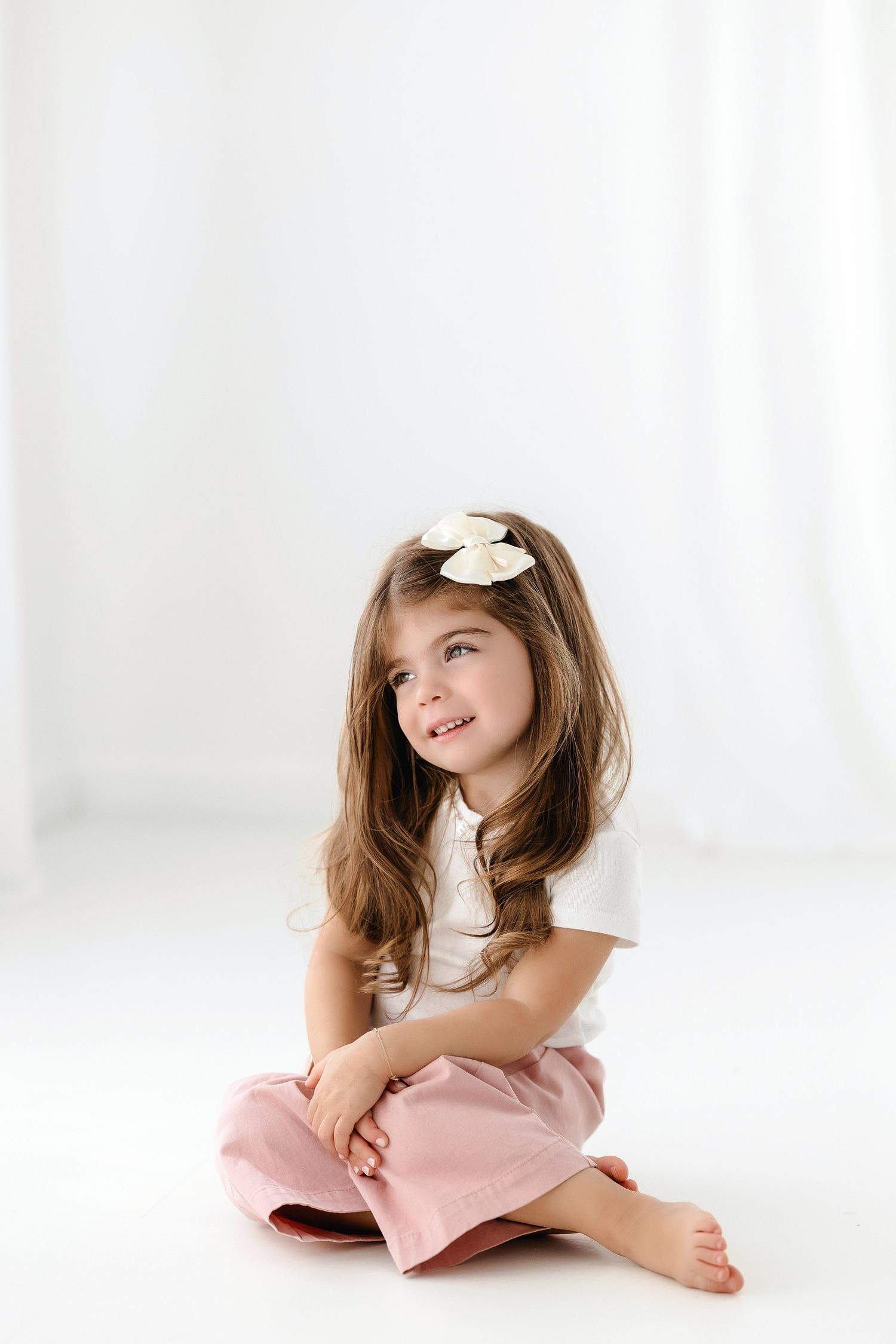 A child in a soft pink dress poses playfully on a white backdrop in three artistic portrait shots.