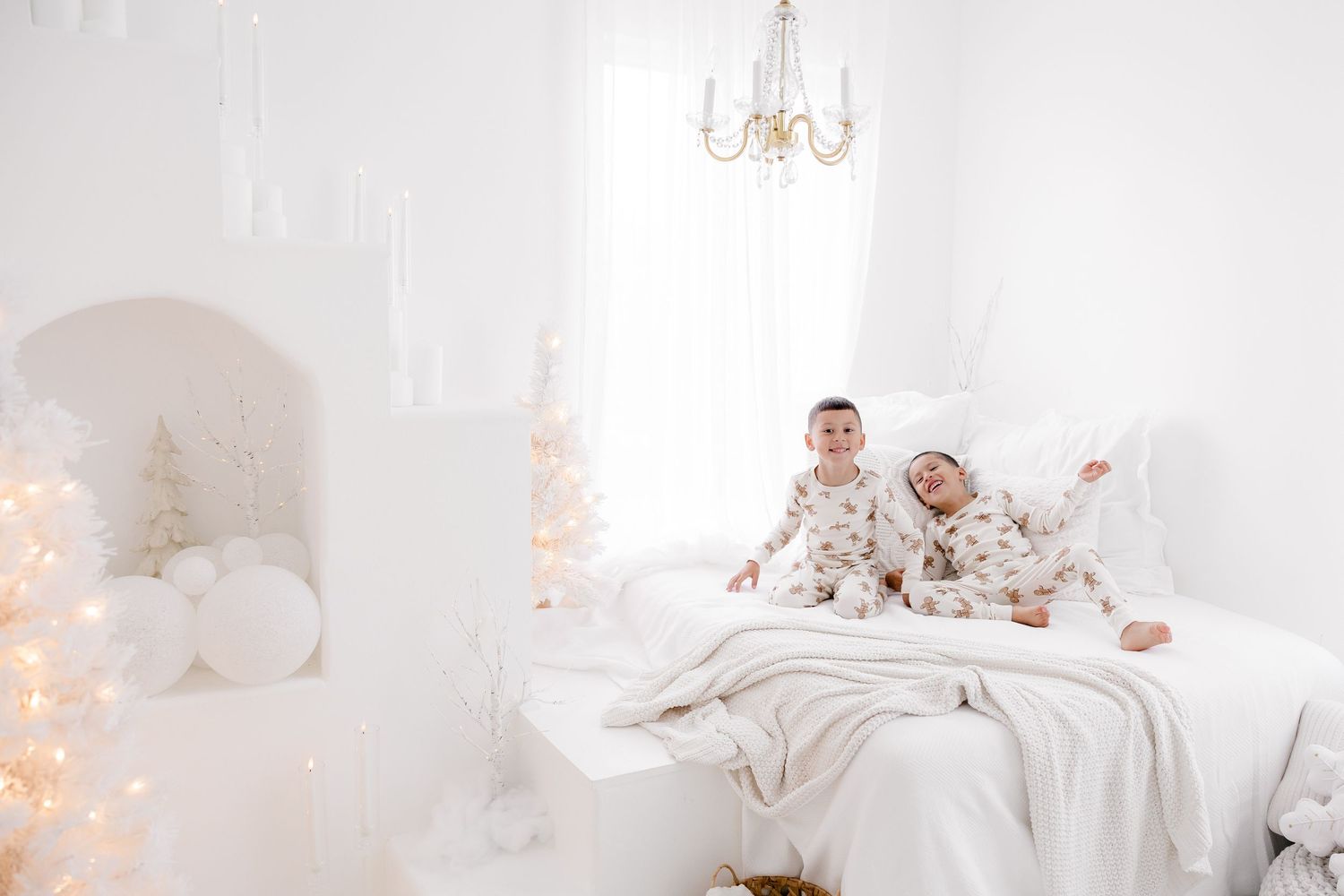 A couple relaxes on a white bed surrounded by Christmas decorations and twinkling lights.