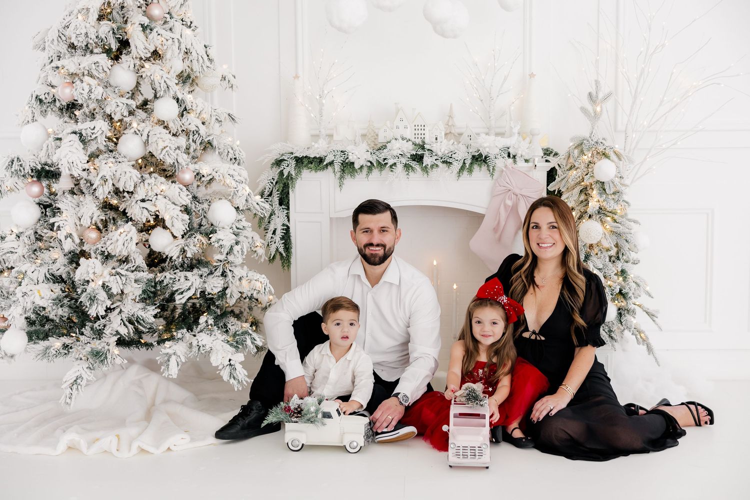 Family sitting together by decorated white Christmas tree in elegant holiday photo setting.nj holiday mini sessions