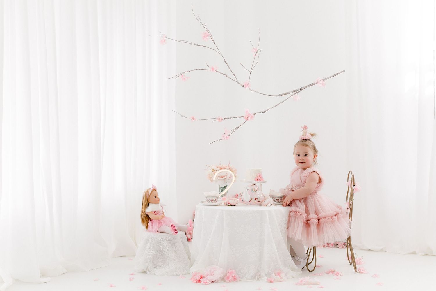 Child's pink tea party setup with delicate branches and white backdrop.