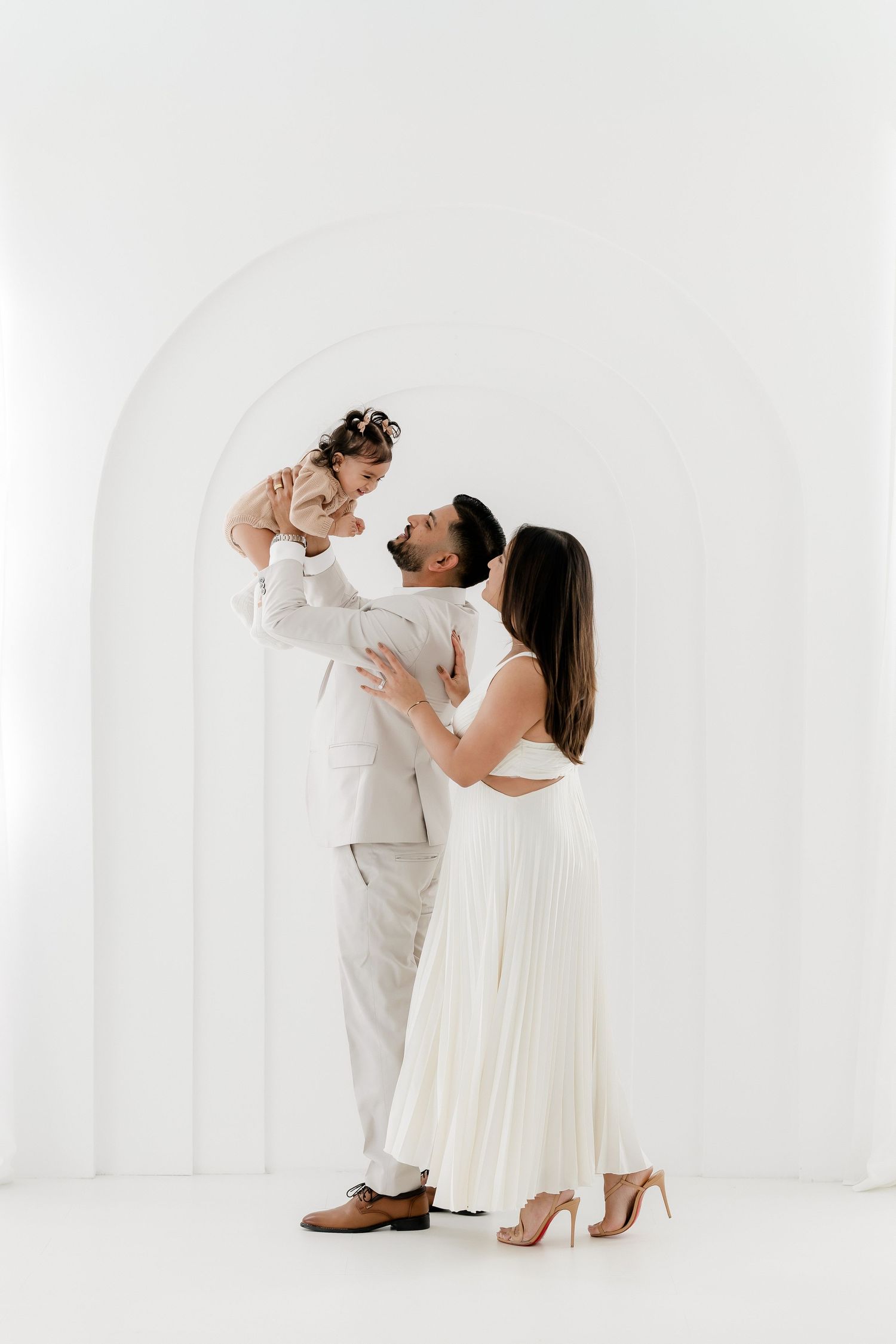 Parent and baby in matching white outfits share joyful moments during studio photoshoot against white backdrop.