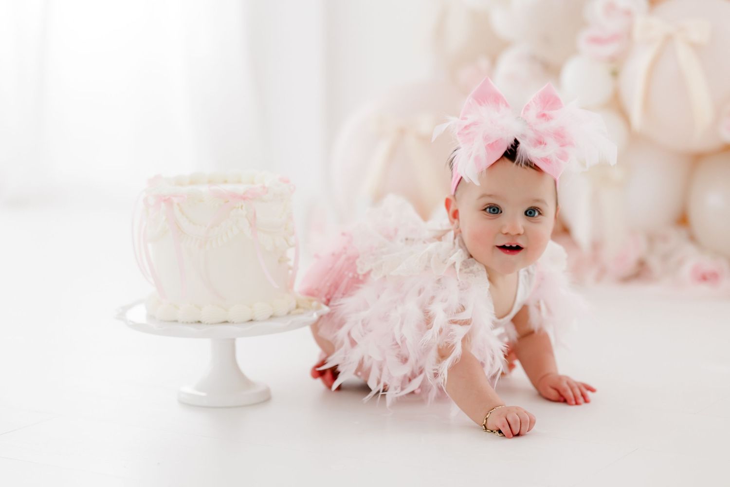White cake on pedestal with pink tulle decor in soft pastel studio setting.