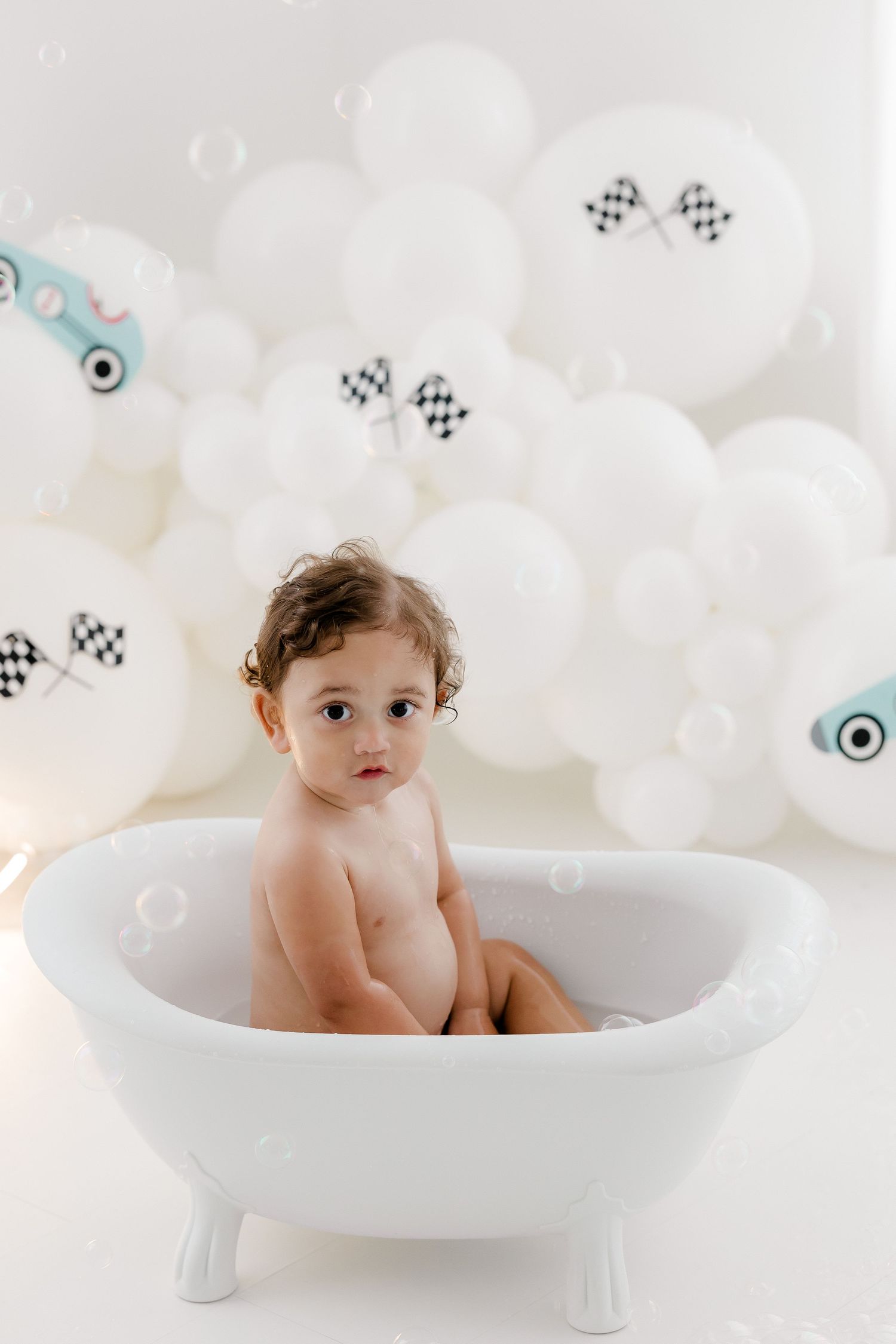 White bathtub photography setup with checkered flag decorations and bubbles in a bright studio.