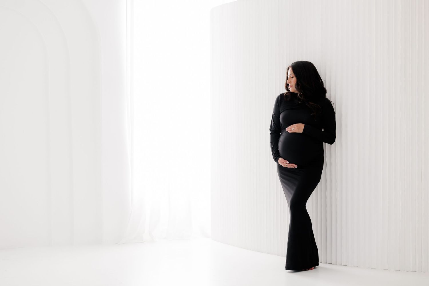 Modern maternity portraits in black dress against minimalist white backdrop.
