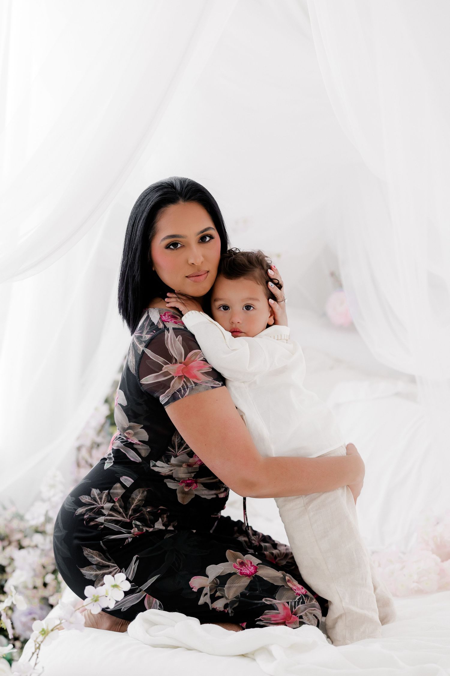 A tender moment captured in white with soft lighting showing parent and child embracing on light fabric background.