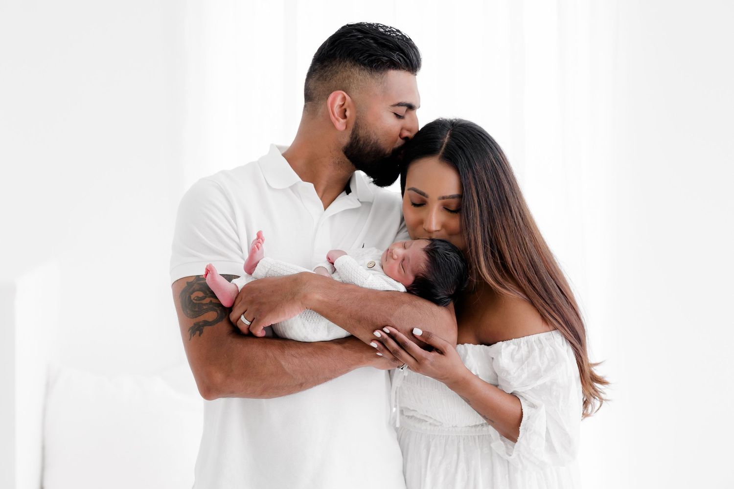 A romantic couple in white clothing embraces tenderly against a light background.