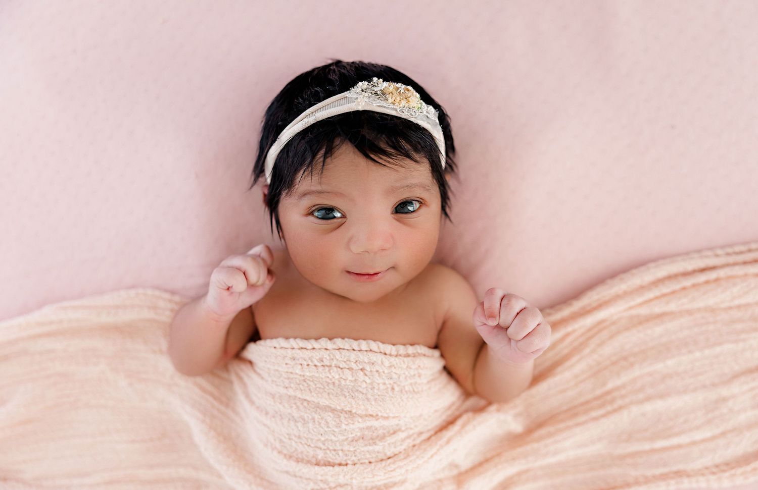 Newborn baby wrapped in soft pink blanket during studio photoshoot.