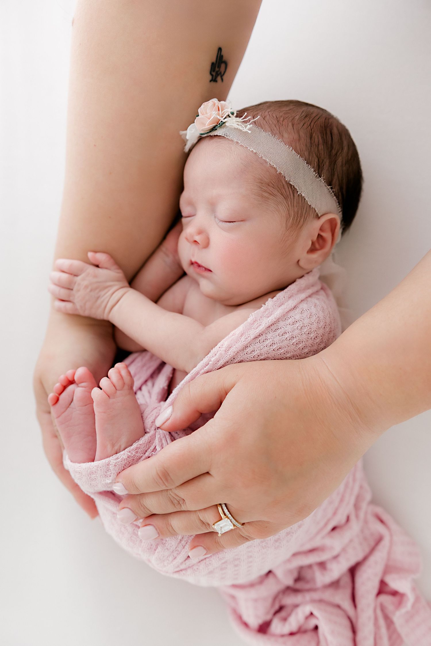 Peaceful newborn baby sleeping while wrapped in pink blanket and white headband.