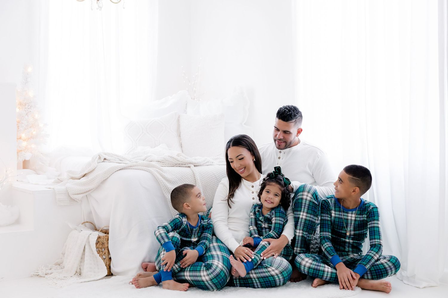 Family members in matching plaid pajamas share tender moments in a white studio holiday setting.