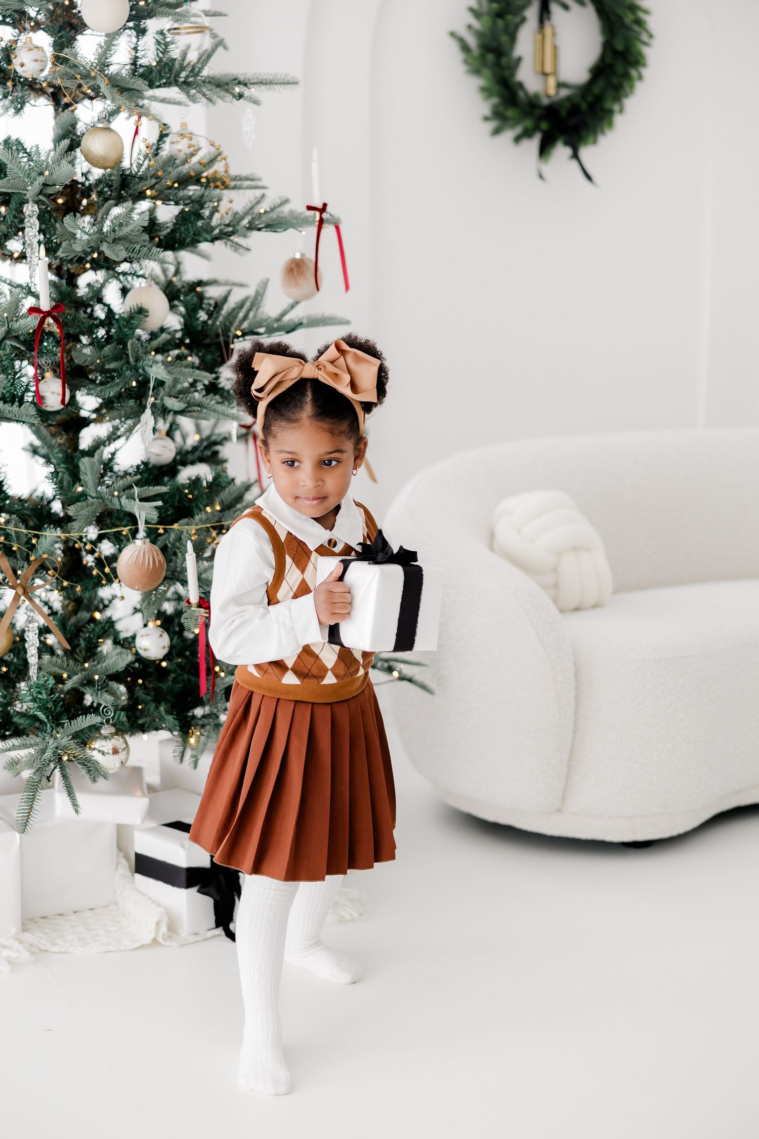 Holiday portrait setup with a Christmas tree and white furniture in a minimalist studio.