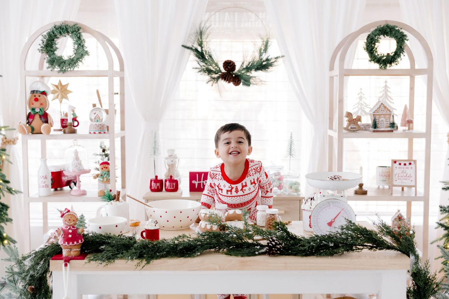 Modern white studio decorated with Christmas wreaths, evergreen trees, and red accents creates a festive holiday backdrop.