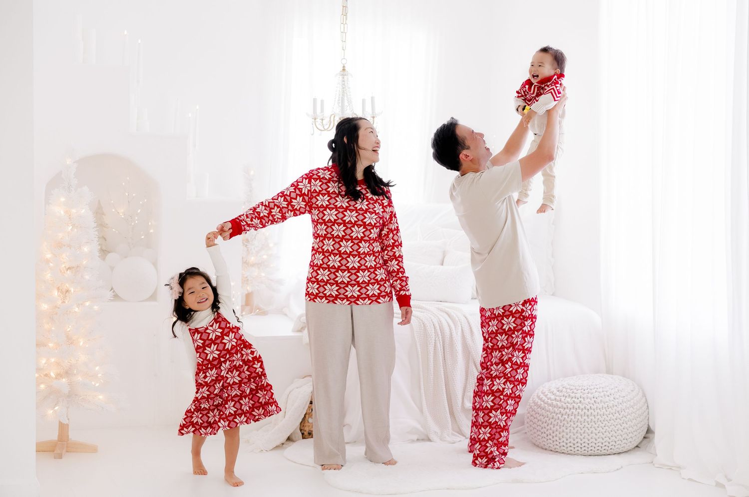 Family wearing coordinating holiday outfits poses in bright white studio with Christmas tree.
