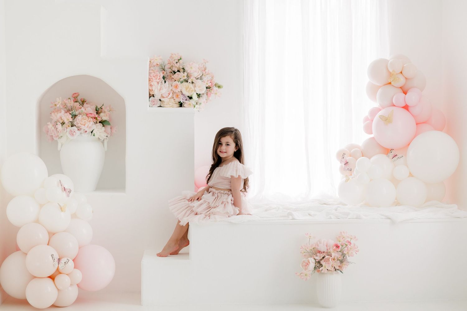 Soft pink and white balloon garlands and floral decorations create a dreamy romantic backdrop for photos.