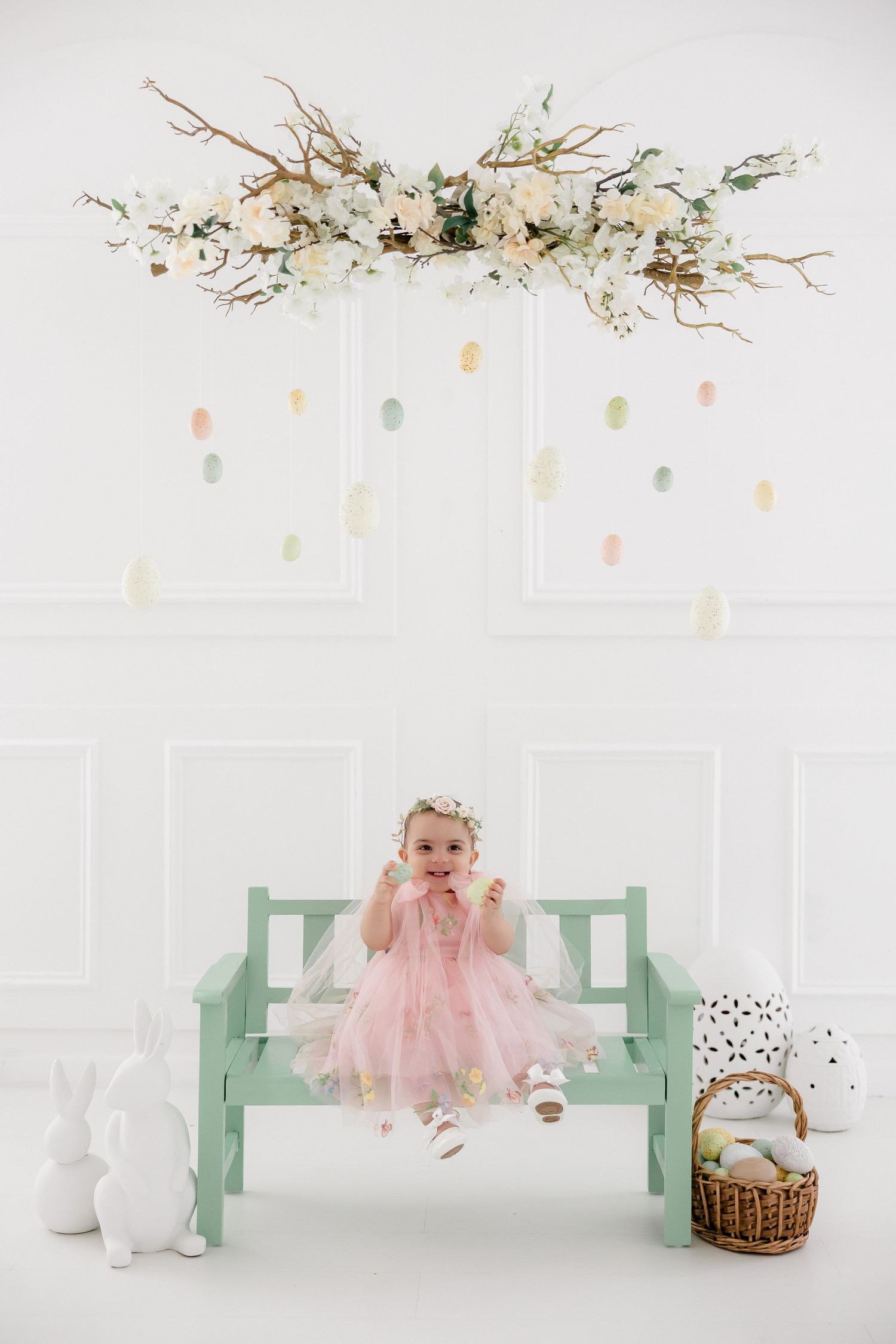 Minimalist white studio setup with mint green bench and delicate floral decorations for baby photography session.