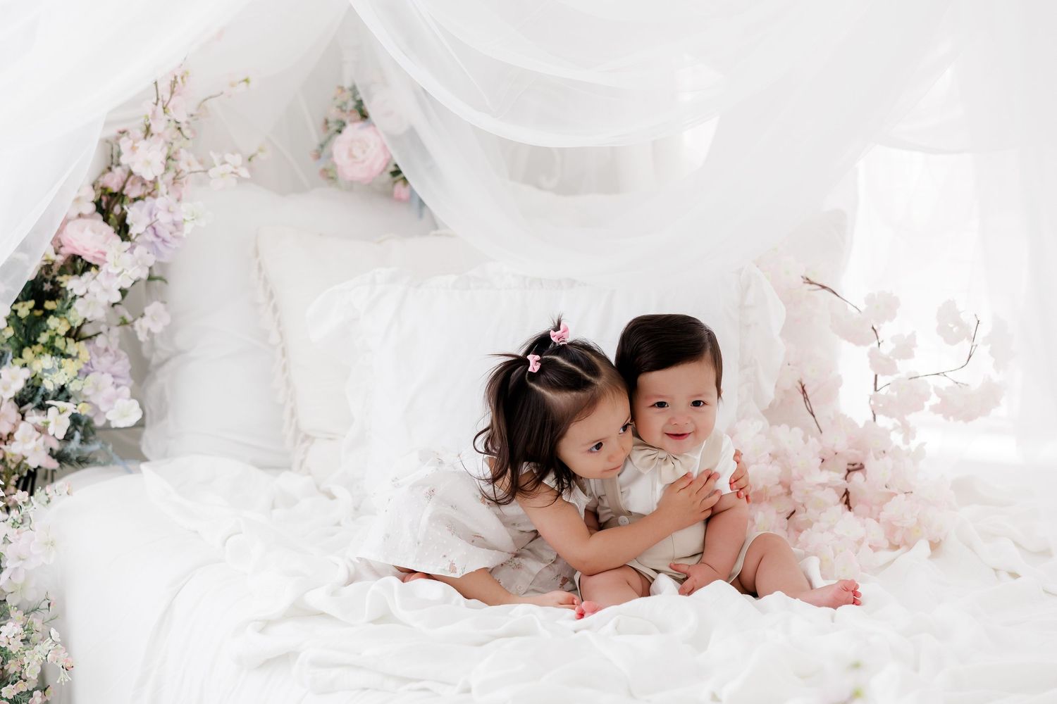 A romantic wedding photo session with soft white tulle fabric and delicate pink floral arrangements in the background.