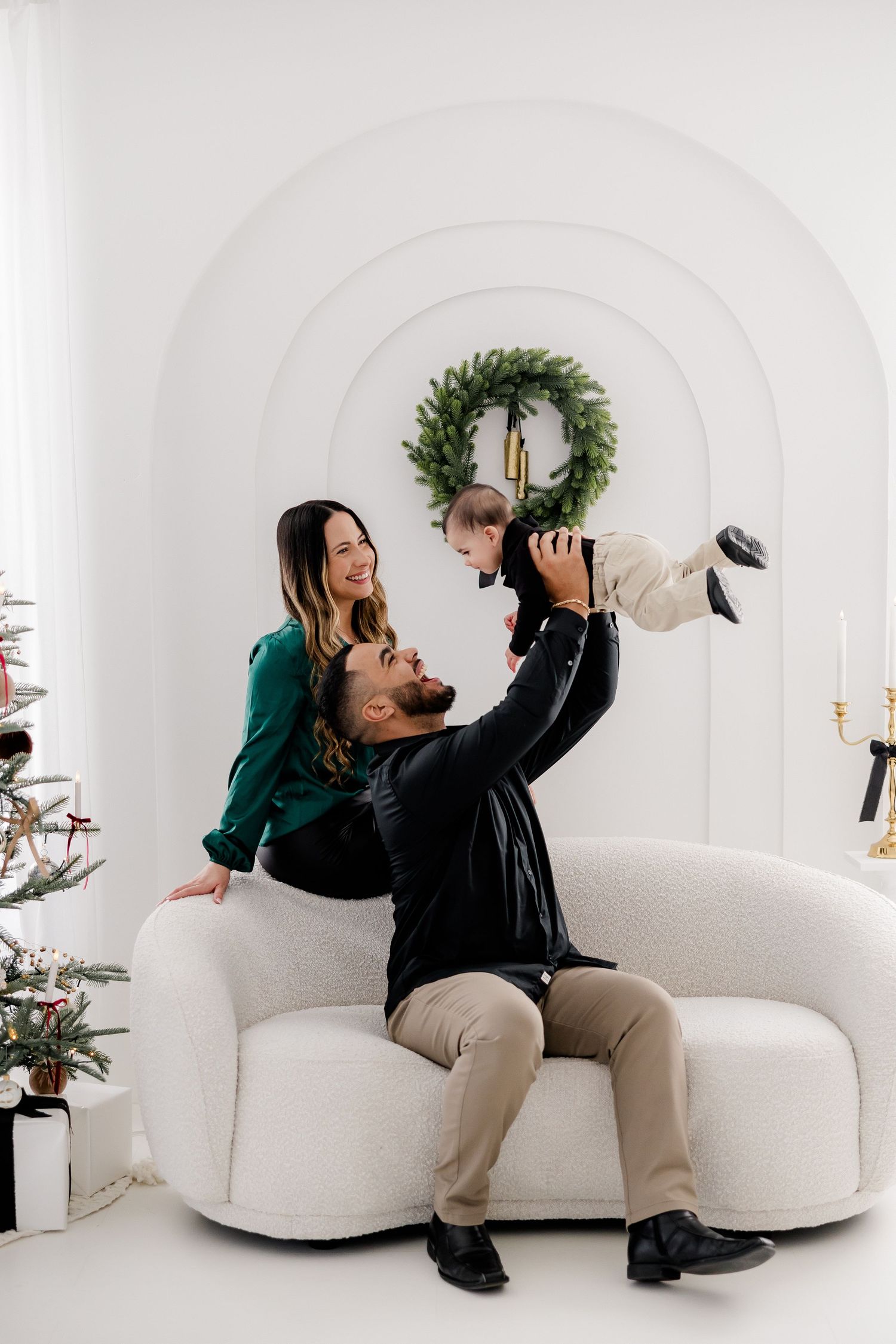 Family playing together on white couch with Christmas tree and wreath in background.
