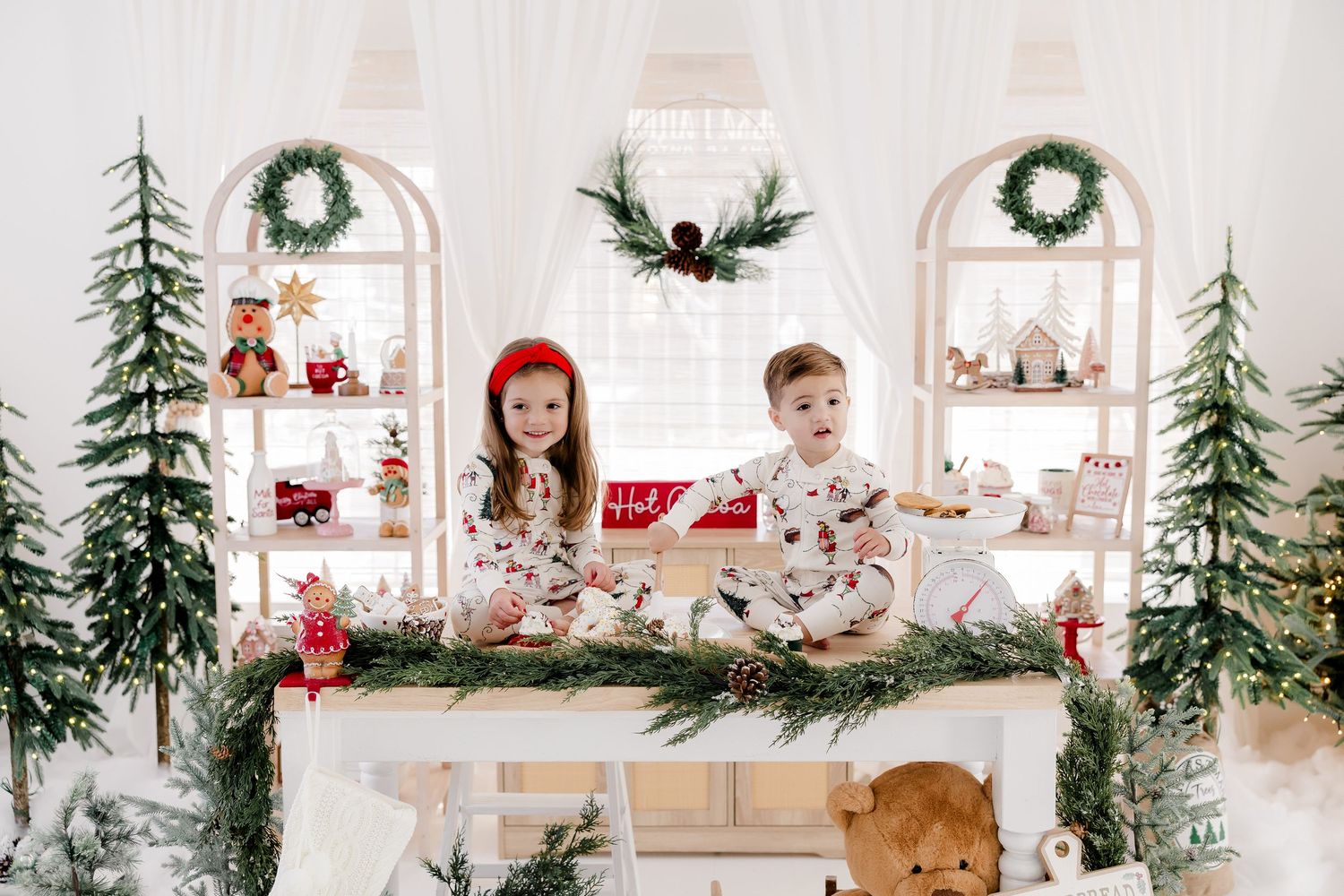 White Christmas studio decorated with evergreen garlands, wreaths, and pine trees in minimalist style.
