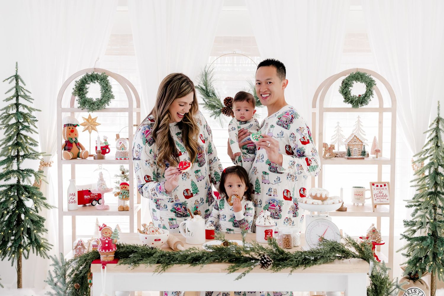 Bright white Christmas photography setup with decorated trees, wreaths, and festive holiday decor.