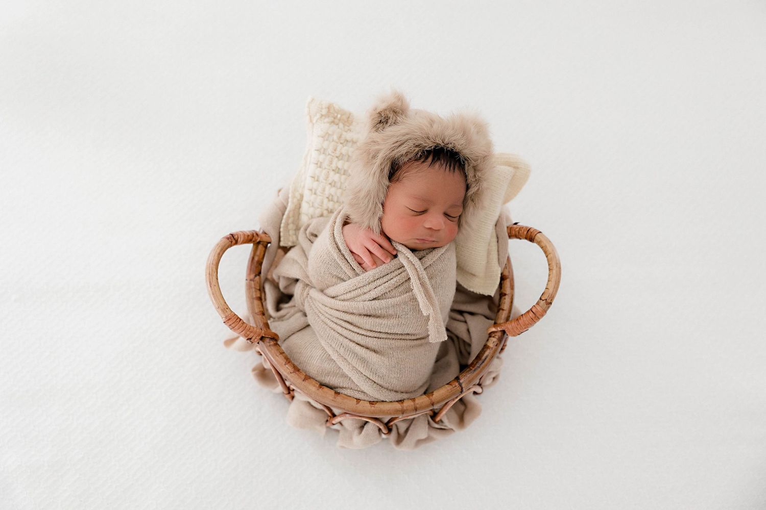 Overhead view of sleeping infant in cream-colored wrap on white surface.