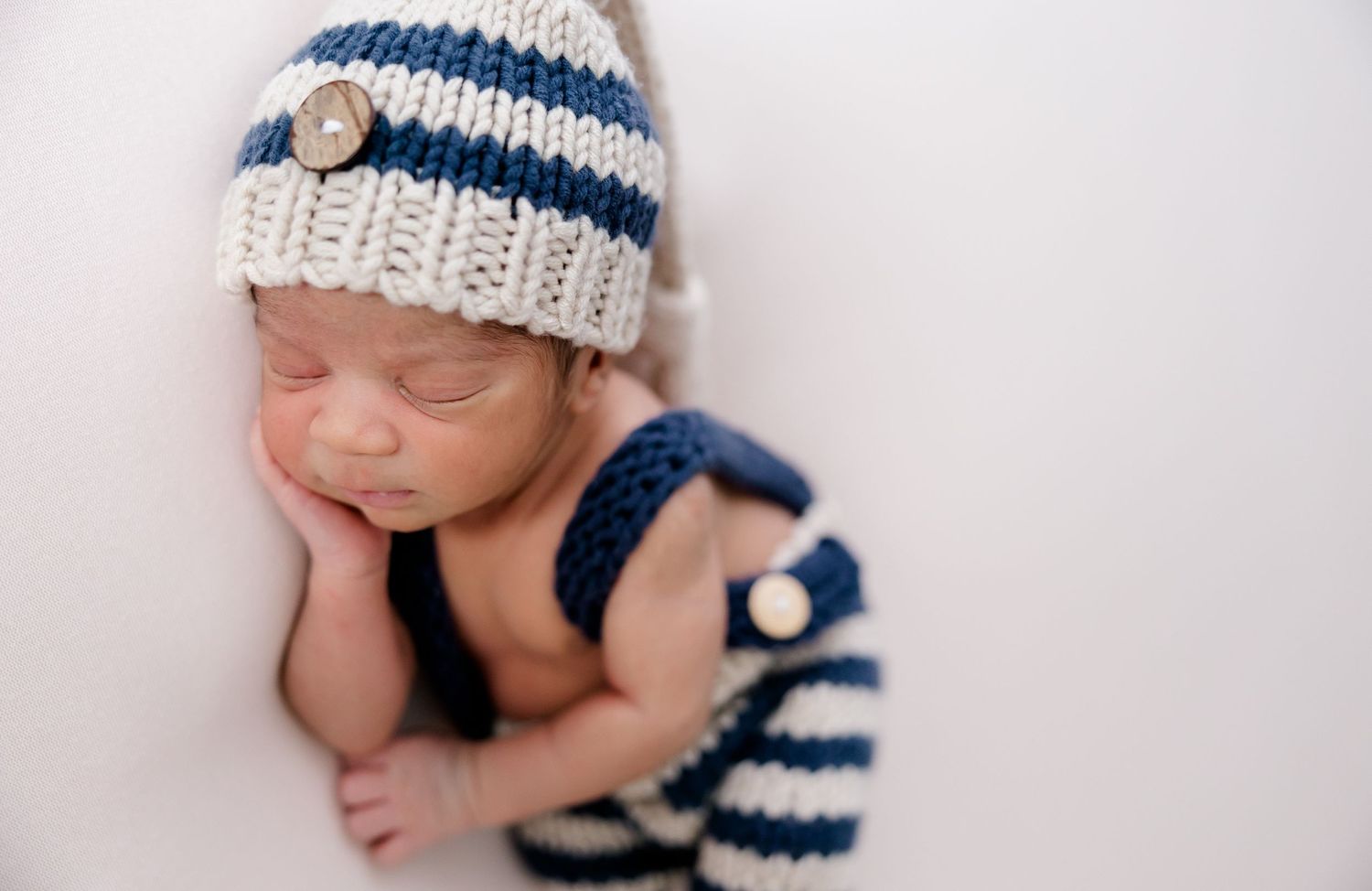Newborn wearing blue and white striped knit hat in a series of peaceful poses.