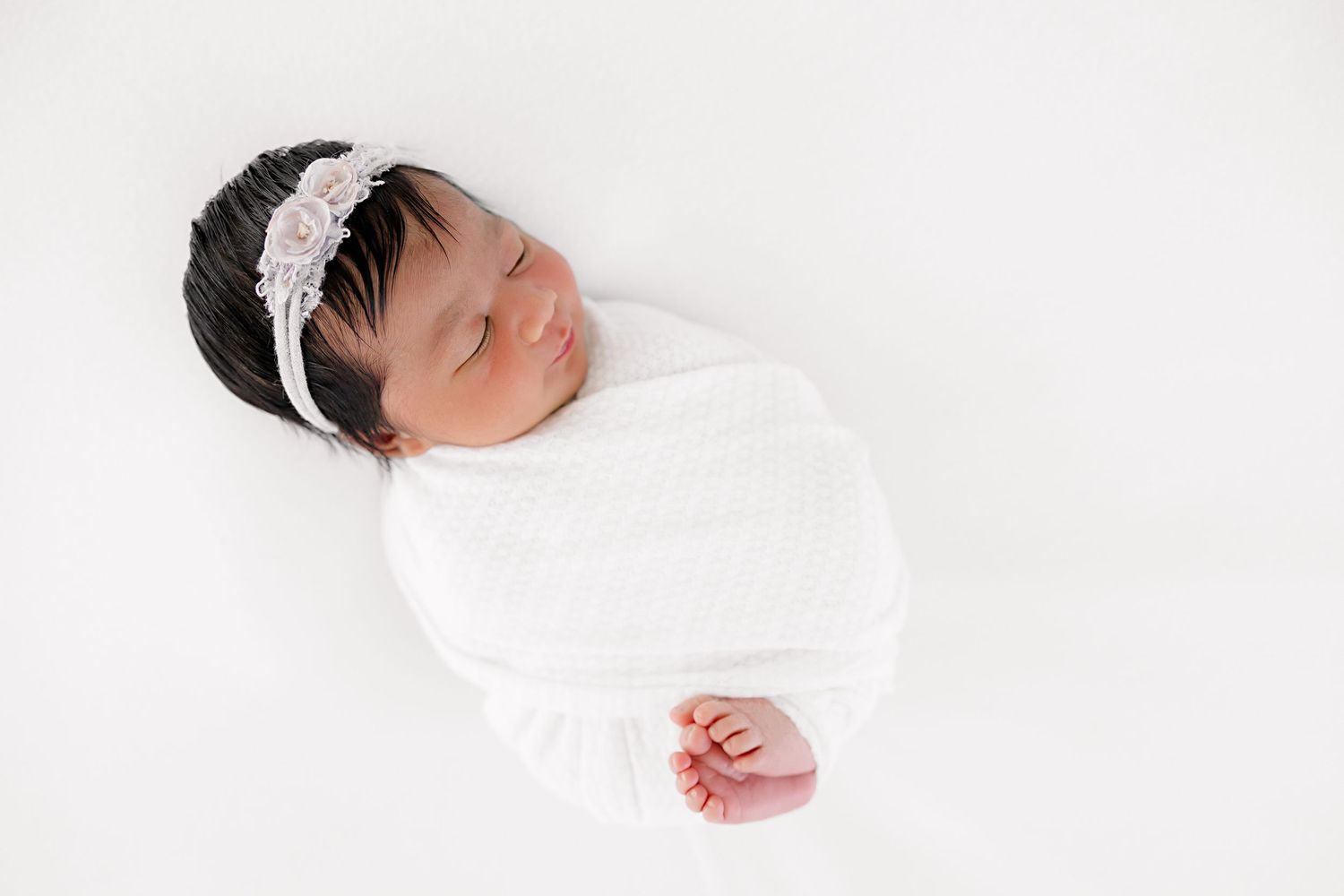 Sleeping newborn swaddled in white fabric against minimalist backdrop.