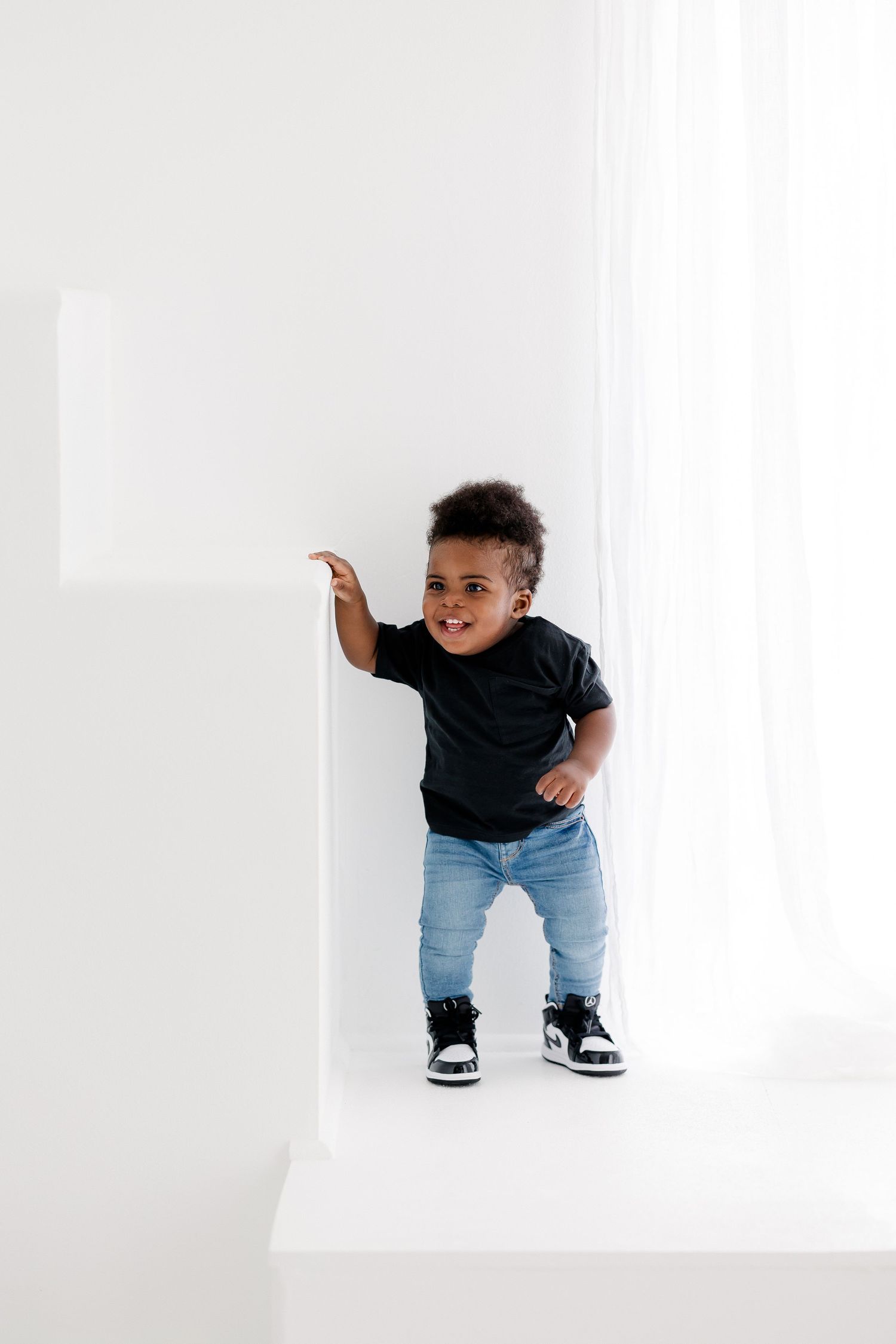 Small child in casual outfit exploring white studio space with geometric cutouts.