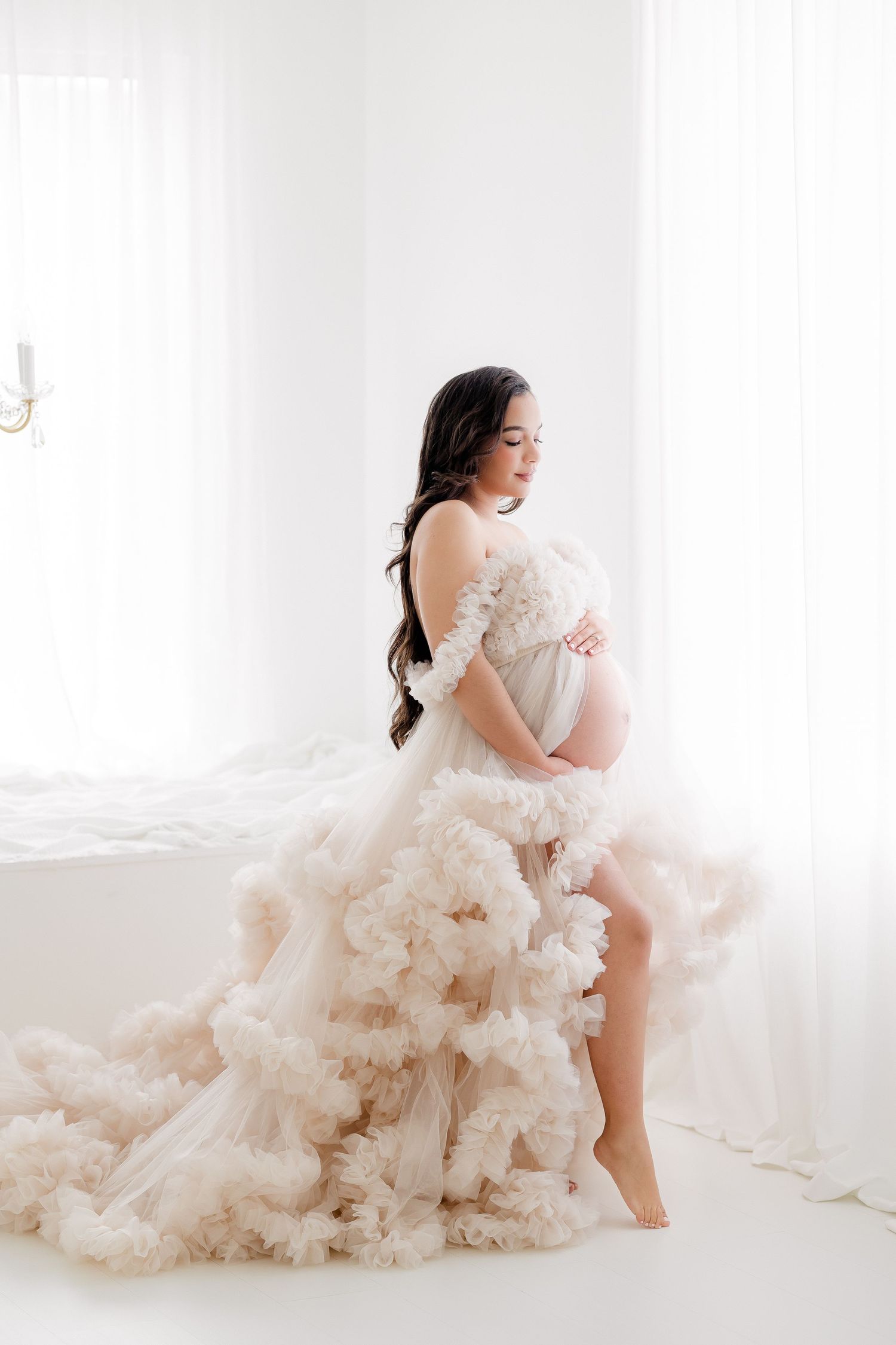 Ethereal blush tulle gown with dramatic ruffles flows across white backdrop in romantic maternity photo session.