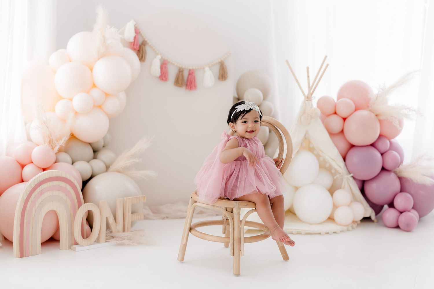Soft pink and white balloon garland with peachy tones creates a dreamy party backdrop against a white wall.