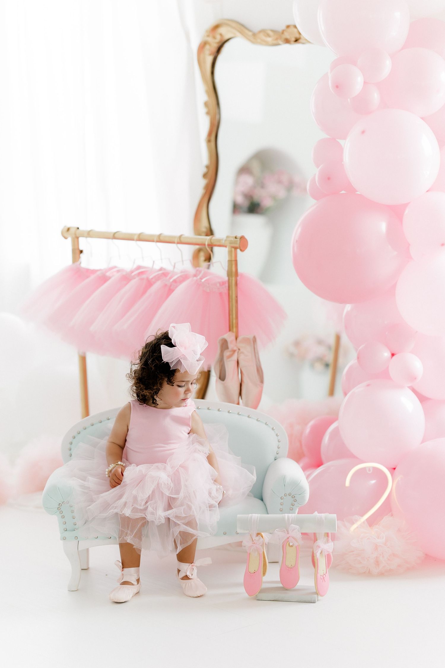 Pink and white cake smash photo session setup with tulle dress, balloons, and vintage style decorations.