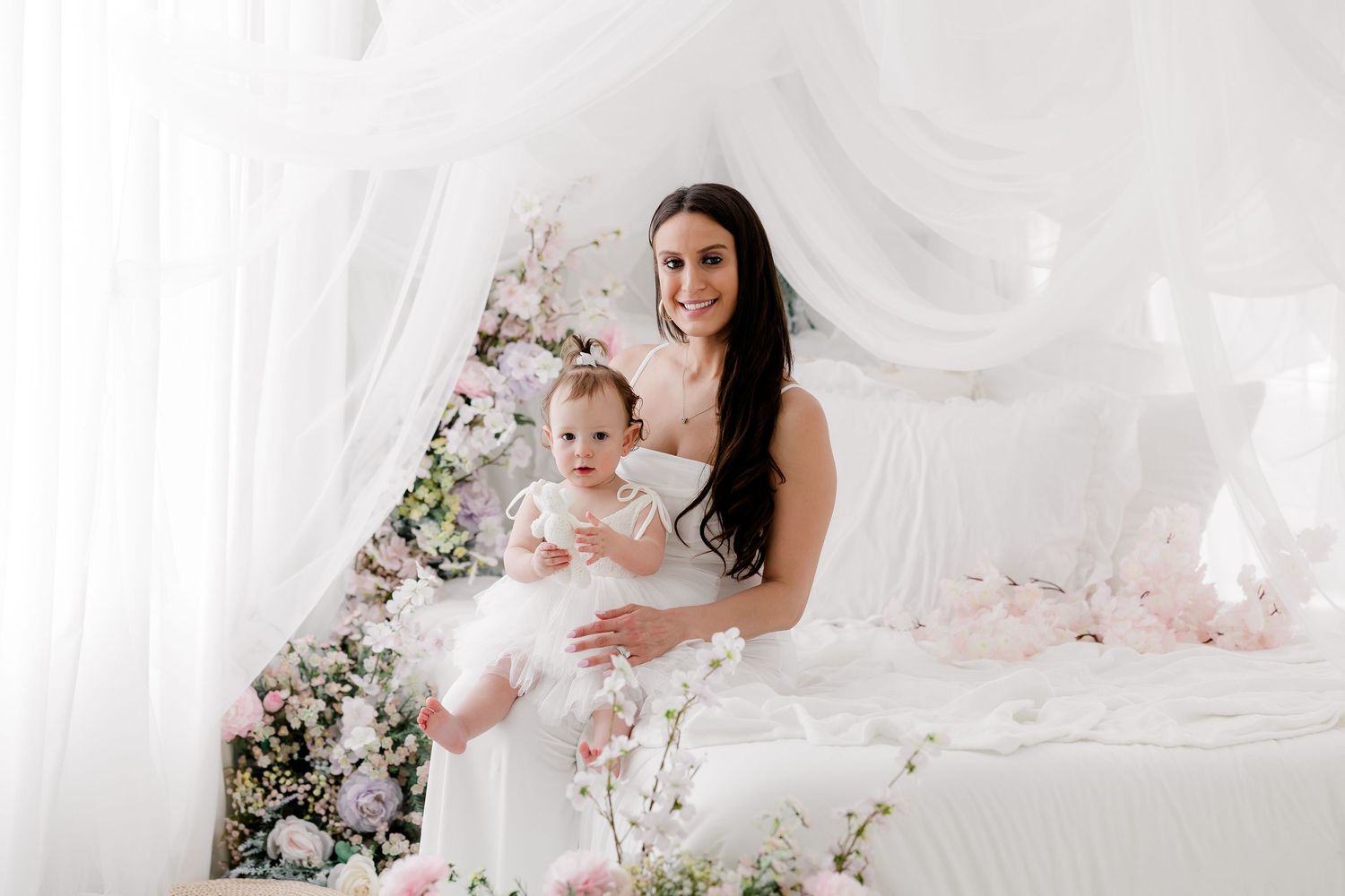 Elegant portrait in soft white setting with flowing fabric and delicate pink cherry blossoms creating a dreamy atmosphere.