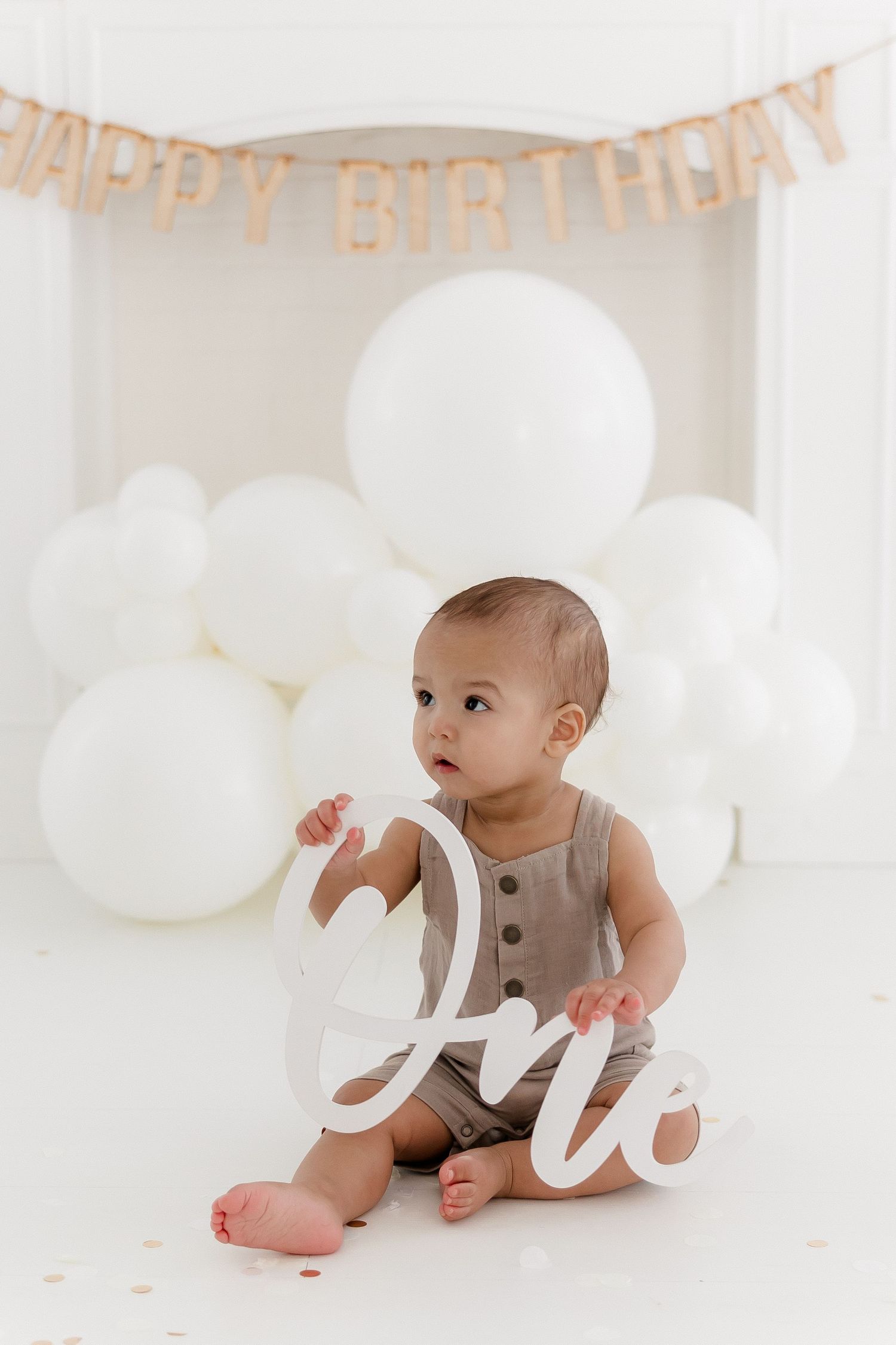 First birthday photoshoot with gray outfit and white balloon decorations.