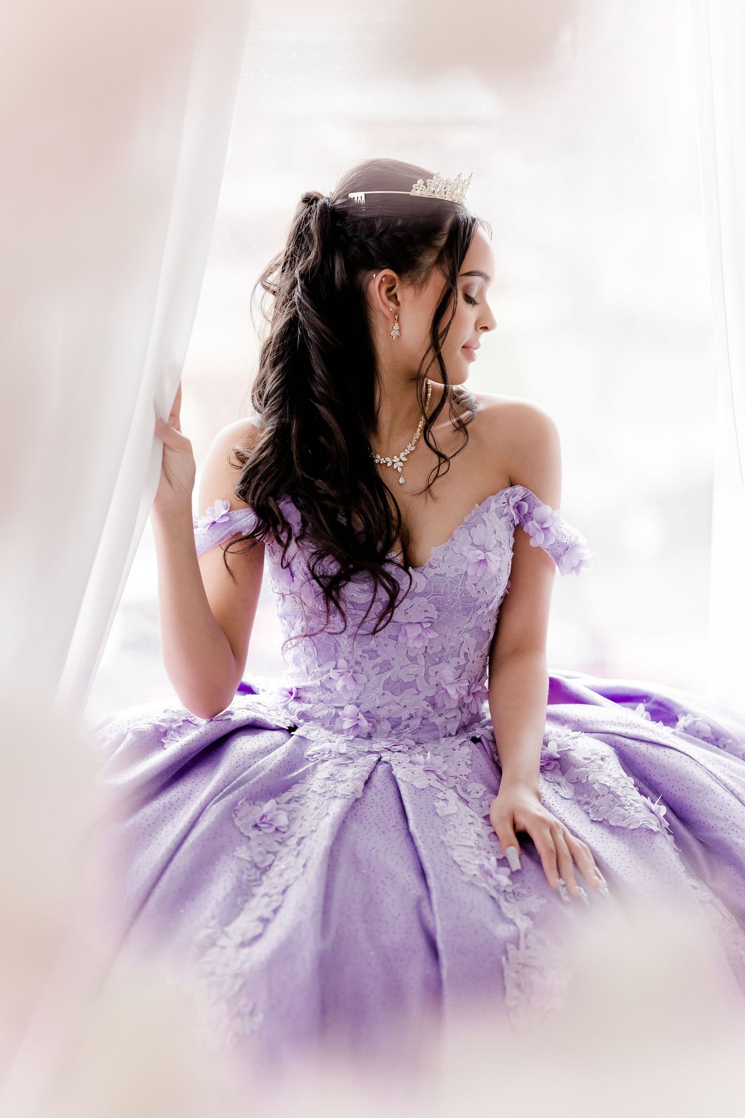 A stunning lavender quinceanera ball gown with delicate lace details and off-shoulder design is showcased in soft lighting.