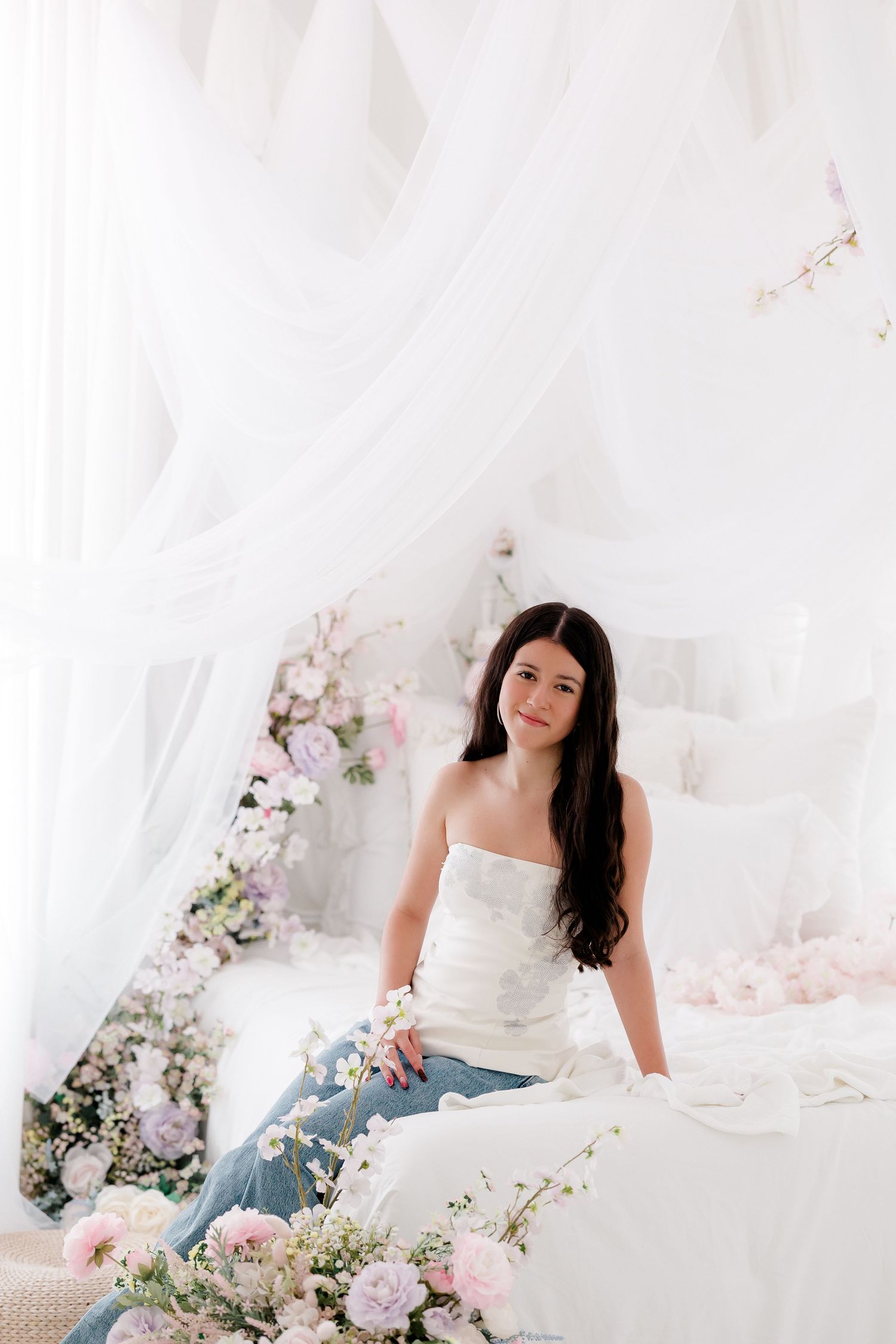 Ethereal bedroom scene decorated with delicate pink and white flowers, flowing white fabric draping from above, and soft bedding.