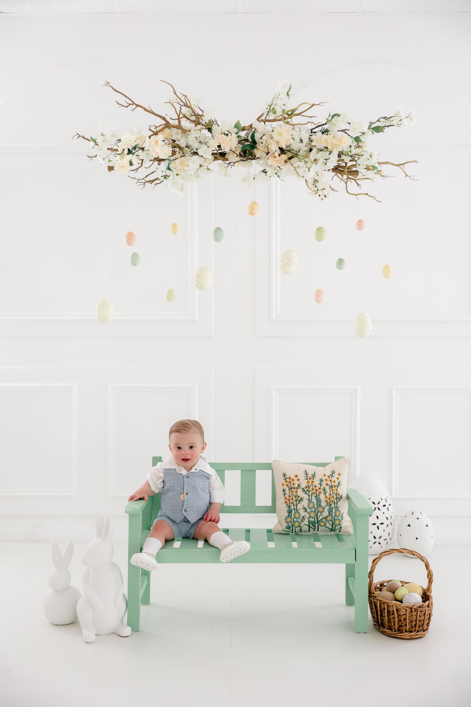 A mint green bench decorated with delicate spring branches and Easter decor against a white backdrop creates a charming scene.