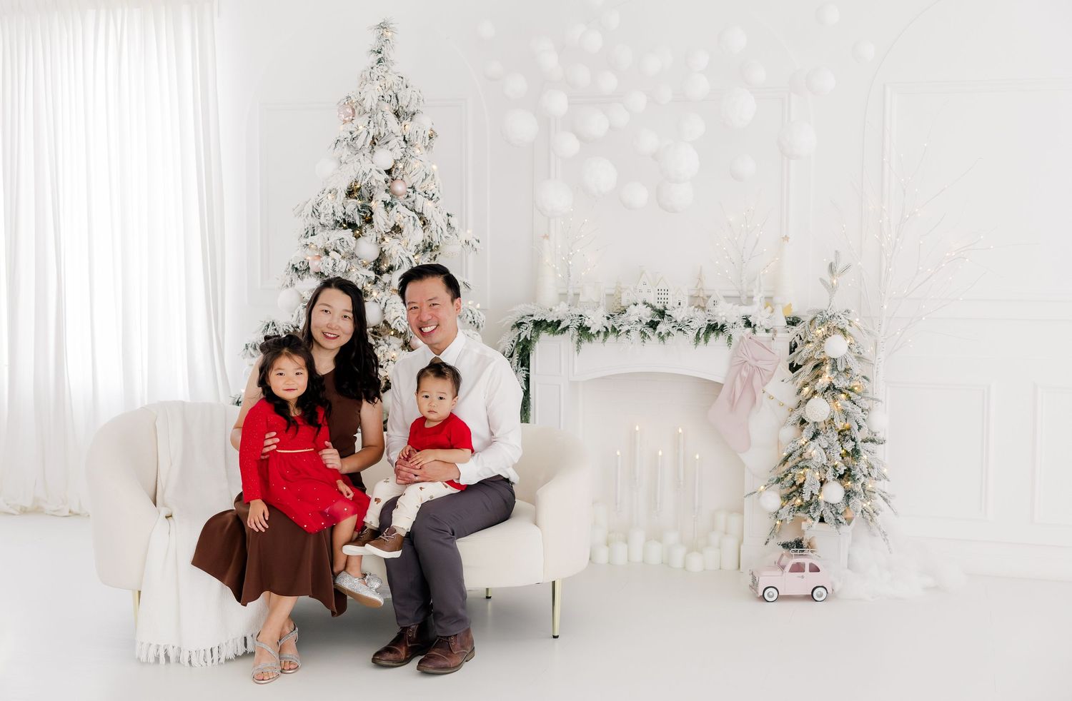 Family celebrates together in white holiday-themed studio with Christmas decorations.