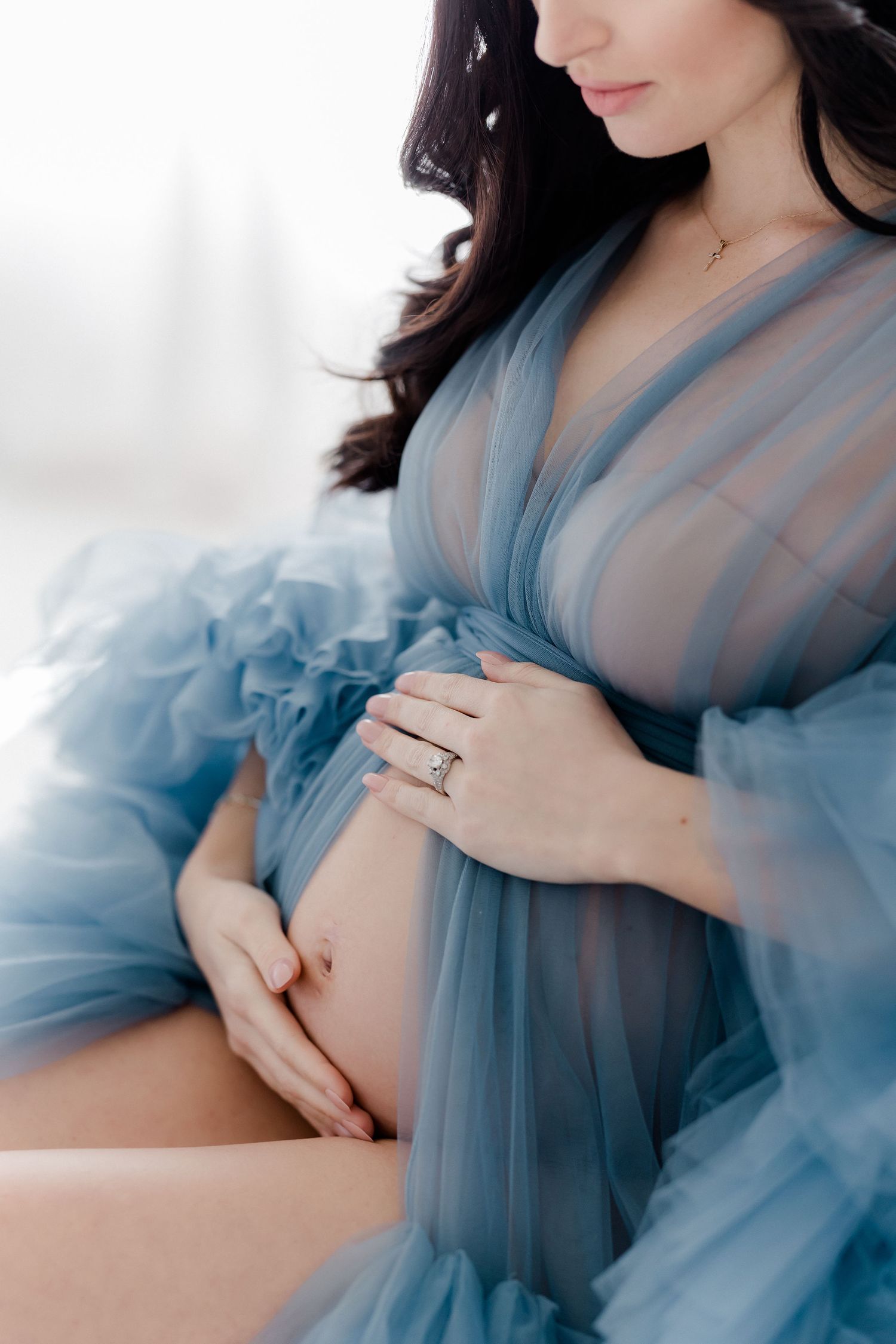 Ethereal maternity photos in soft blue tulle fabric against a light background showcase an intimate moment.