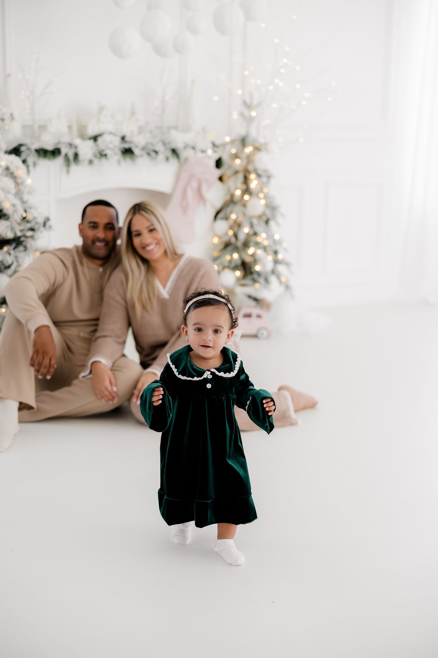 Holiday photo session with a toddler wearing a dark velvet dress in a bright white studio setting.