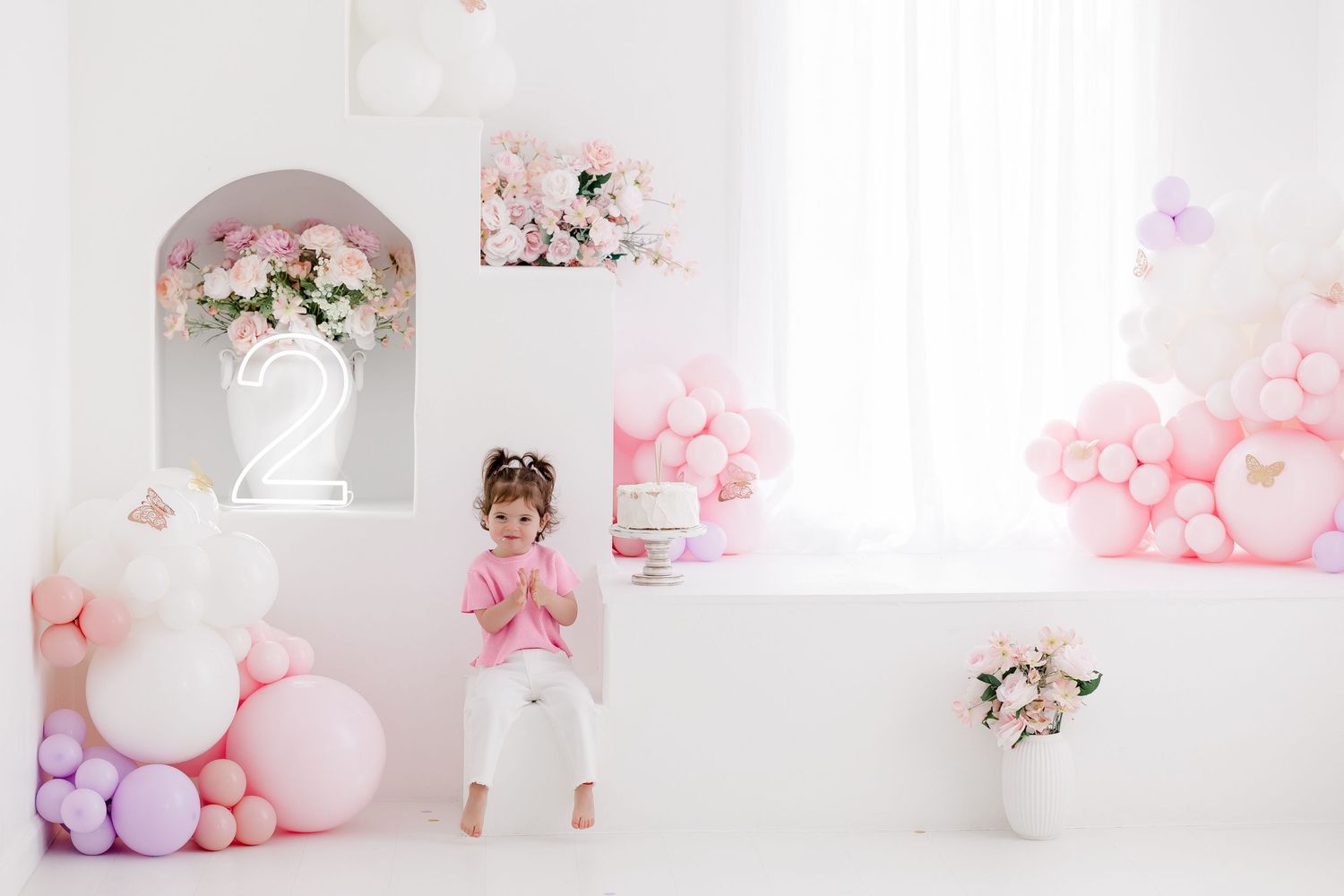 A dreamy pink and white studio setup with balloons, floral arrangements, and soft pastel decorations for photography.