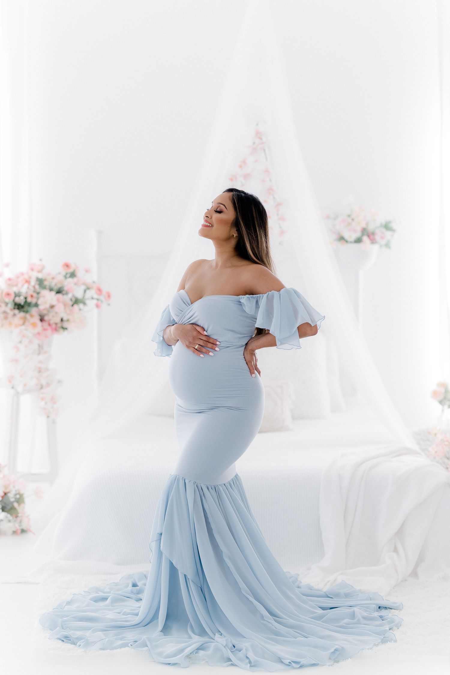 Elegant maternity portraits in flowing powder blue gown against white backdrop.