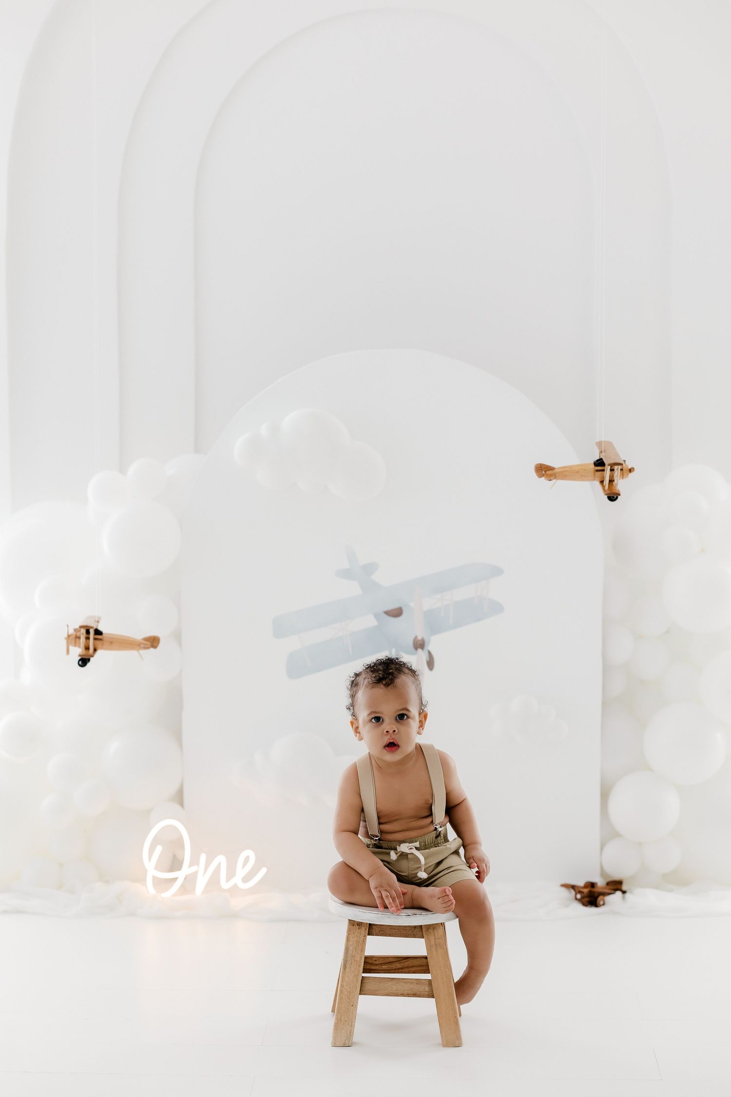 Minimalist baby photography collage with wooden airplane props and white backdrop showing different poses on small chair.