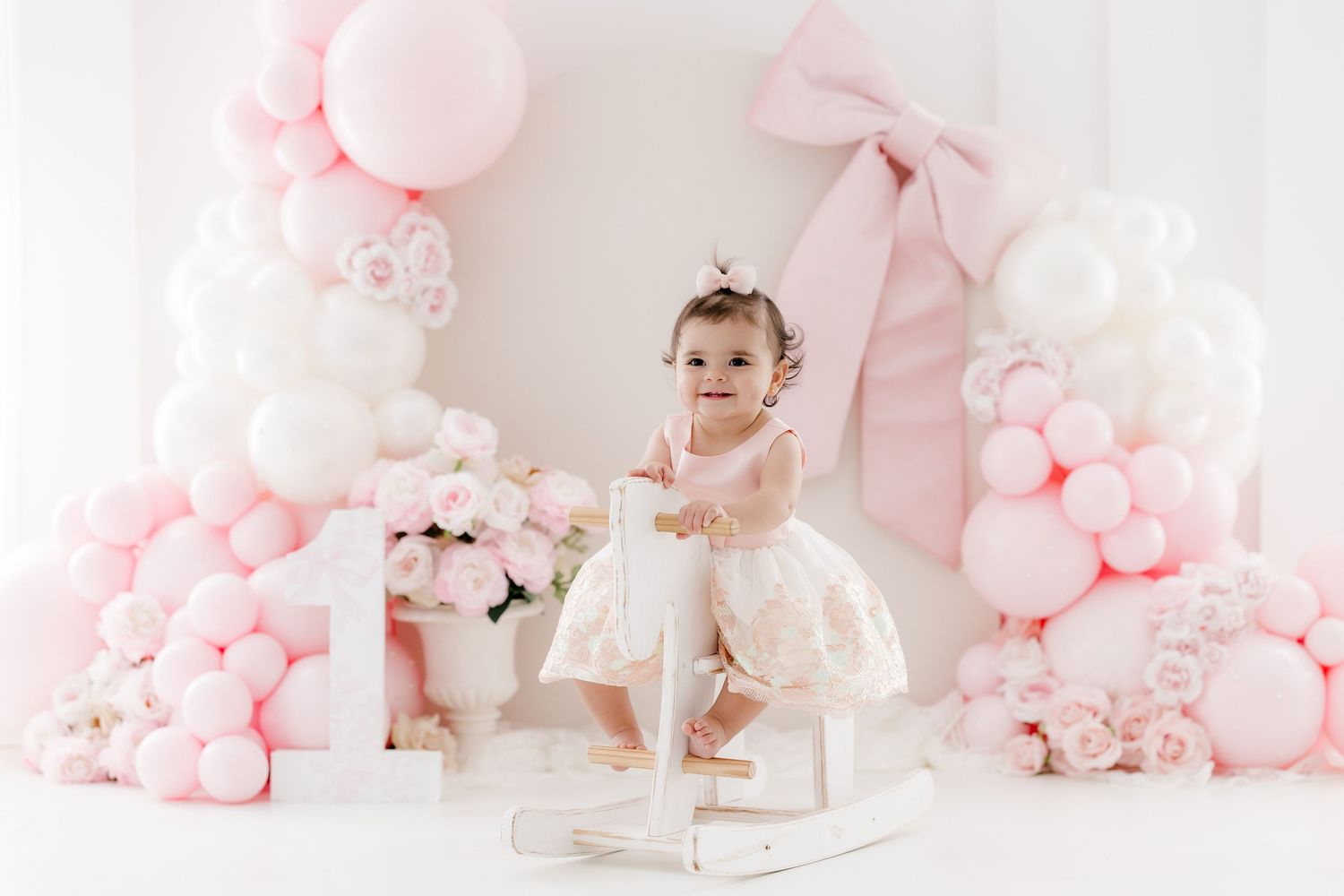 Pink and white balloon decorations create a dreamy backdrop for a first birthday cake smash photo session.