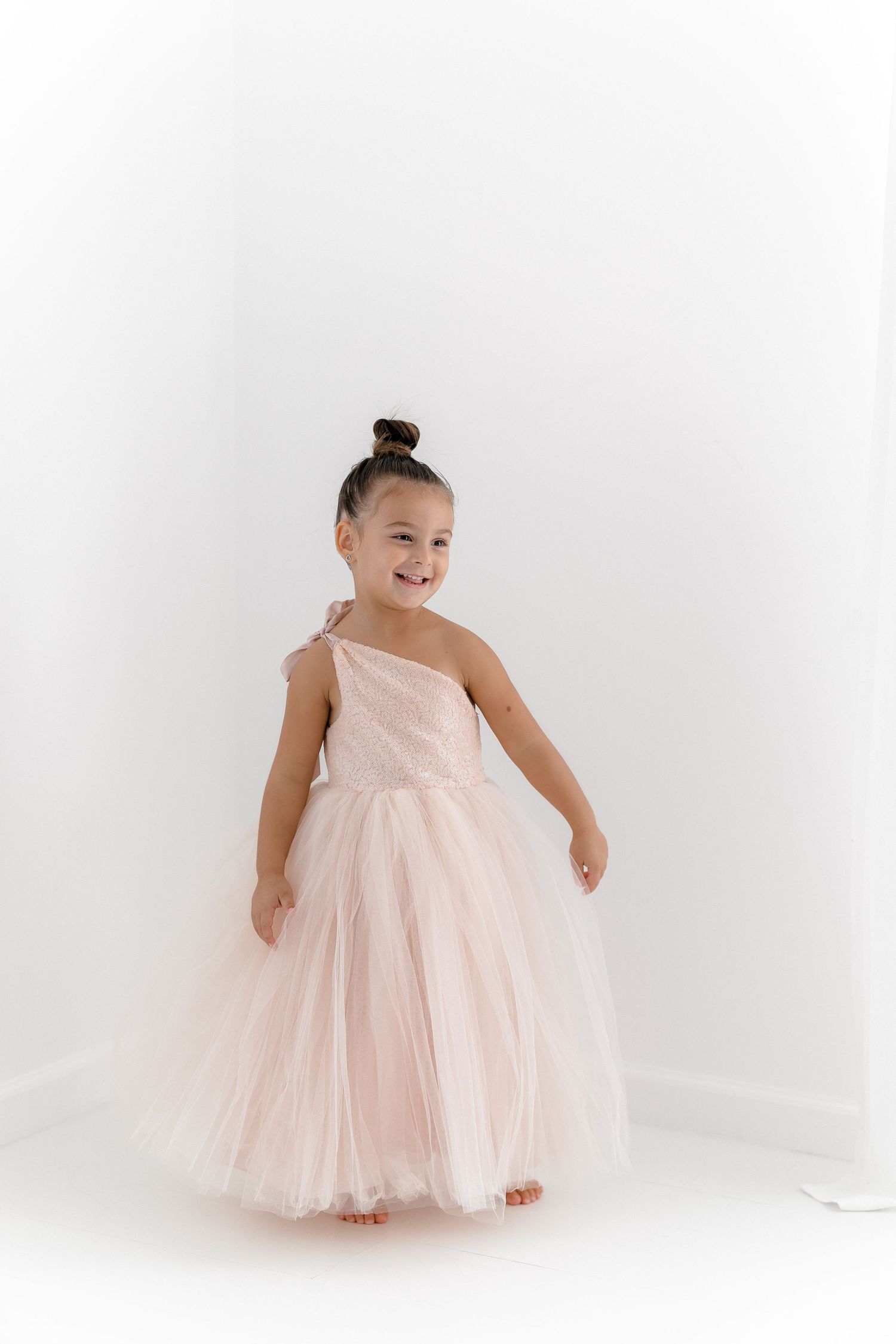 Dancer in pale pink tulle gown strikes joyful pose in bright studio.