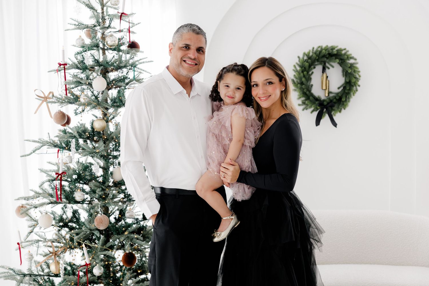 Family holiday portraits captured against a white backdrop with decorated Christmas tree and wreaths.