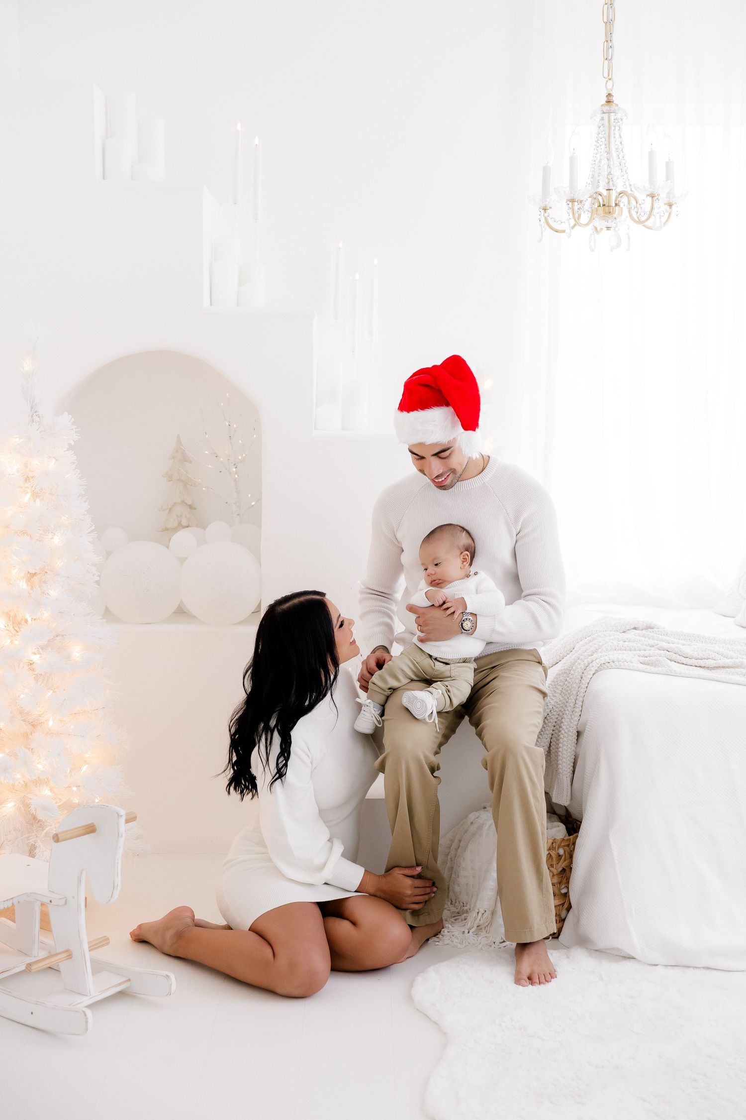 Intimate family Christmas portraits on white furniture with soft lighting and holiday decorations.